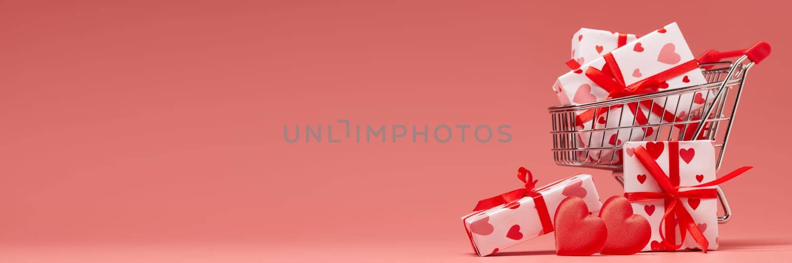 Shopping trolley with gift boxes and red hearts on pink background with copy space. Valentine's Day. Wedding day. Extra wide panorama banner background