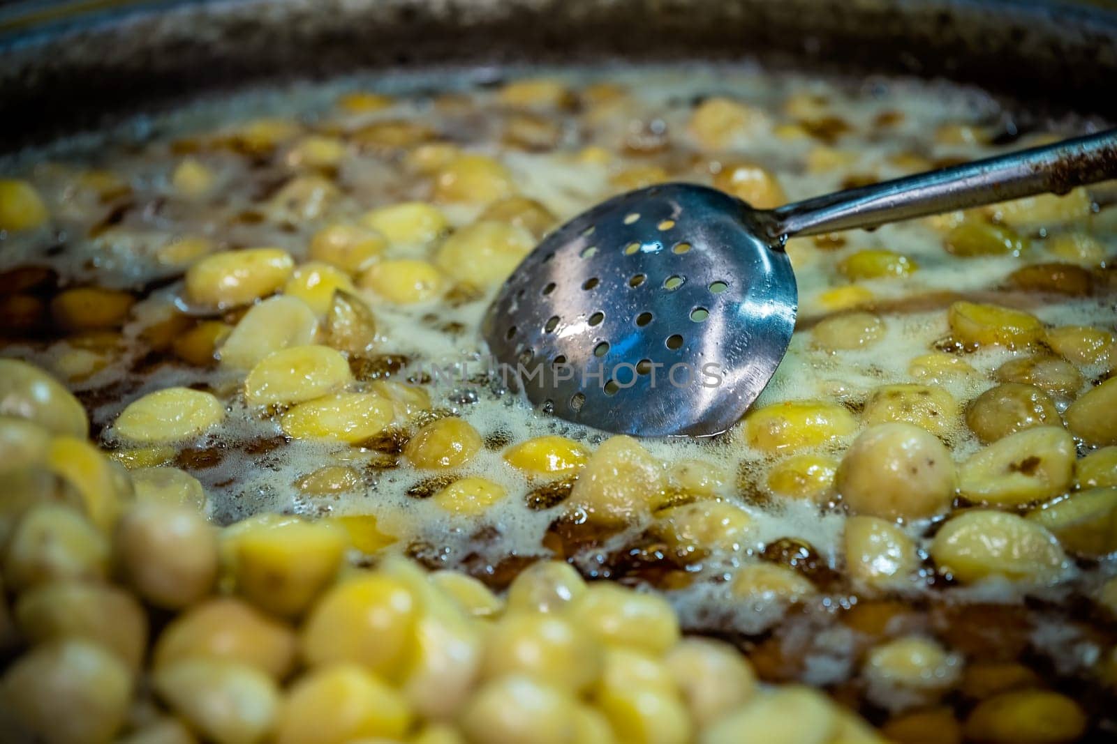 Small cut baby potatoes cooking inside a metal pan full of hot boiling oil on a street food stall in China