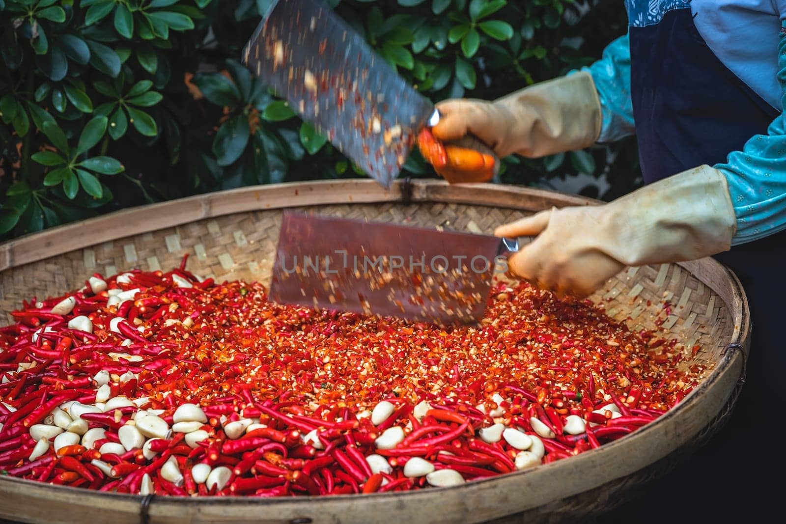 Chillies and garlic being chopped by female worker in a wicker bowl on the street market in Yangshuo town, China