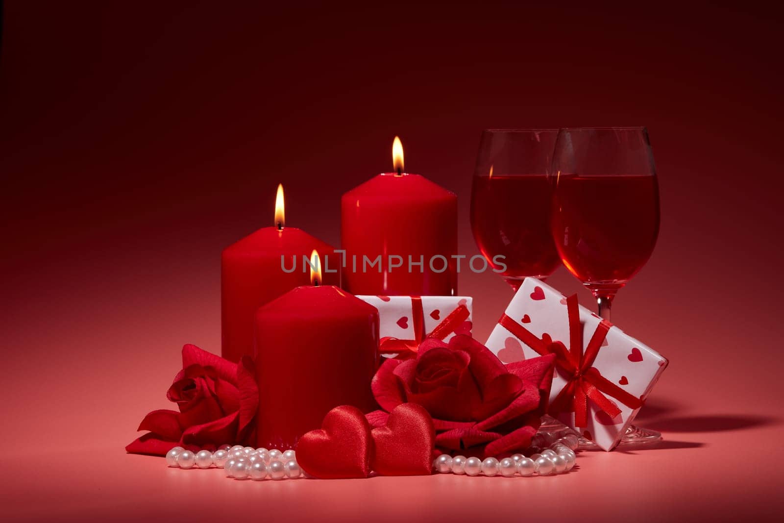 Gift boxes, two glasses with wine, burning candles, red roses and hearts on red background. Valentine's day. Wedding day.  Design element for romantic greeting card and invitation.