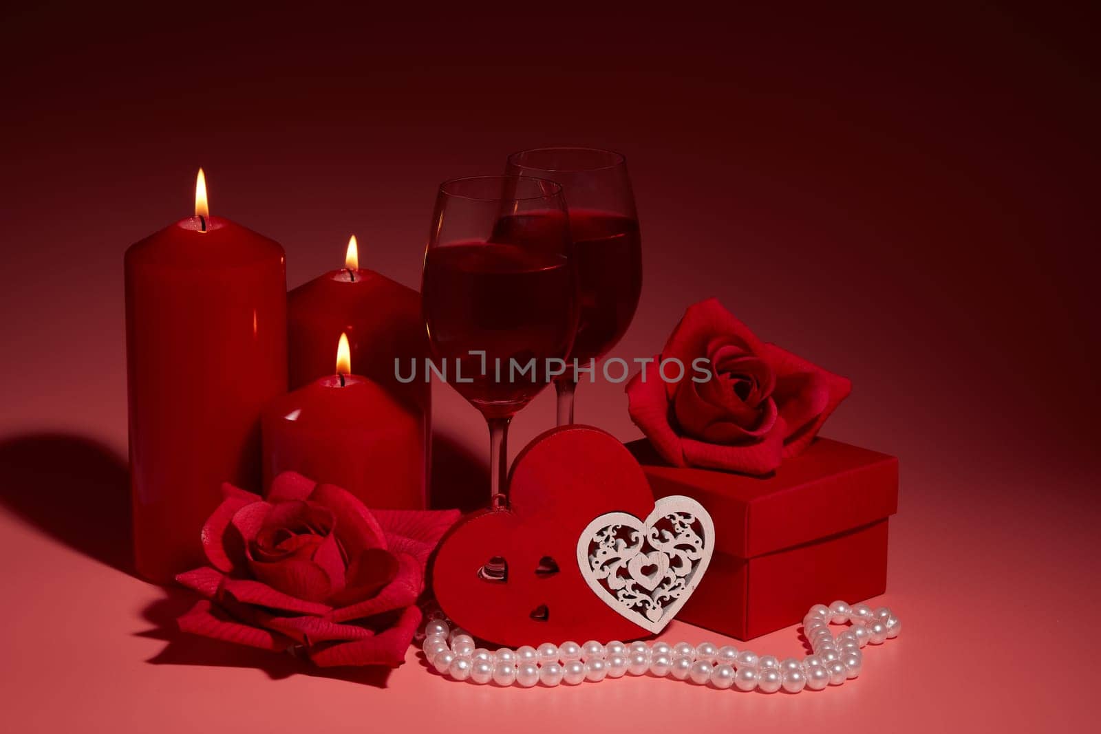 Gift boxes, two glasses with wine, burning candles, red roses and hearts on red background. Valentine's day. Wedding day.  Design element for romantic greeting card and invitation.