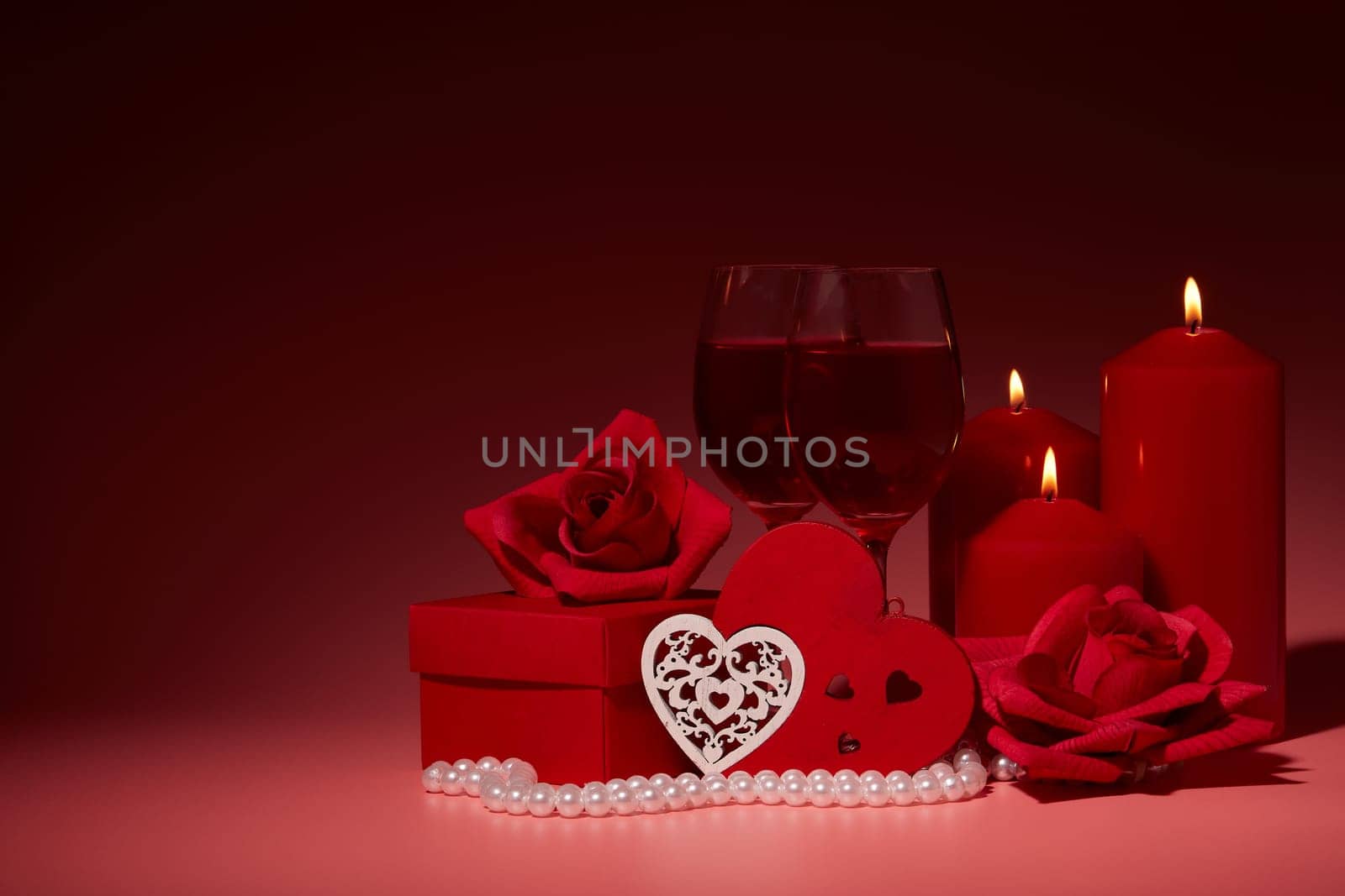 Gift boxes, two glasses with wine, burning candles, red roses and hearts on red background. Valentine's day. Wedding day.  Design element for romantic greeting card and invitation.