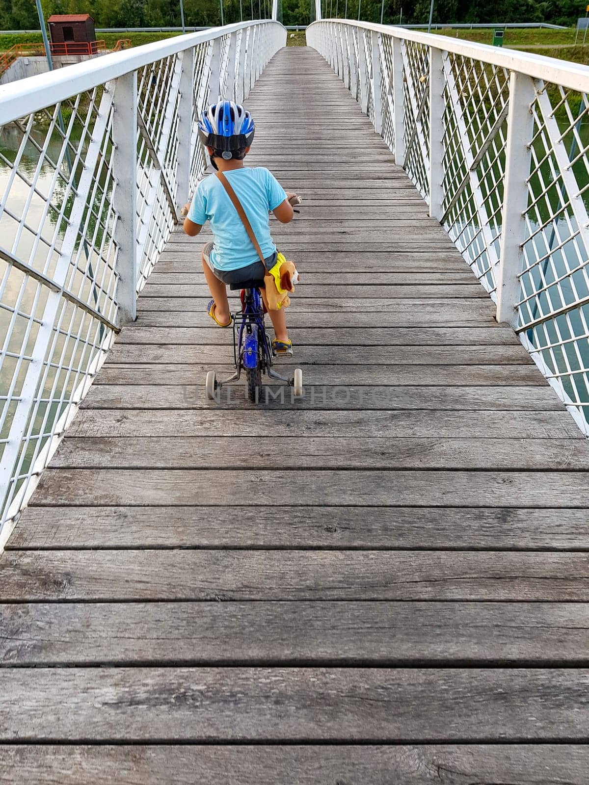 A boy with bicycle on a bridge. The boy has bicycle helmet. White suspension bridge over the river Drava.