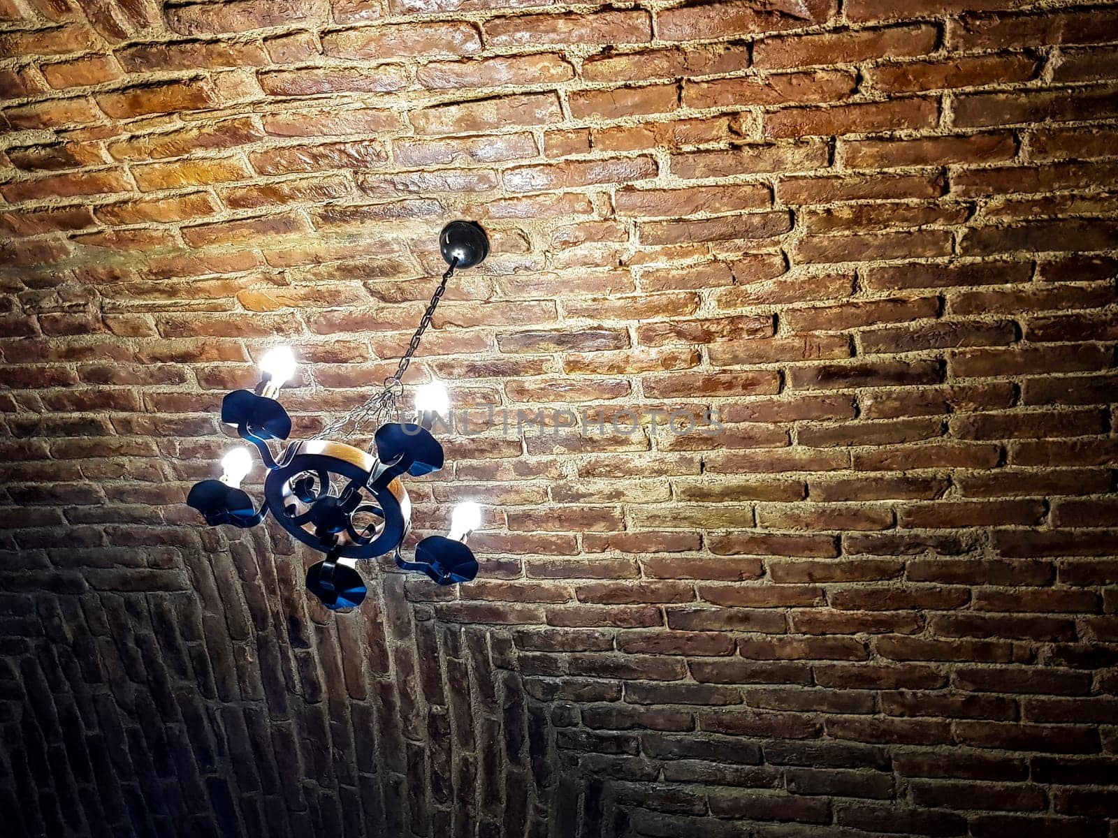 Antique chandelier style with modern lights. It hangs on a red brick ceiling. Rusty look picture.