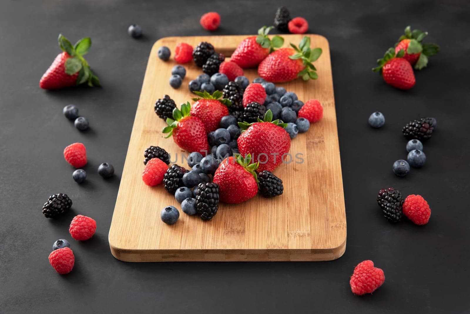 Fresh strawberries, blueberries and blackberries on a wooden cutting board