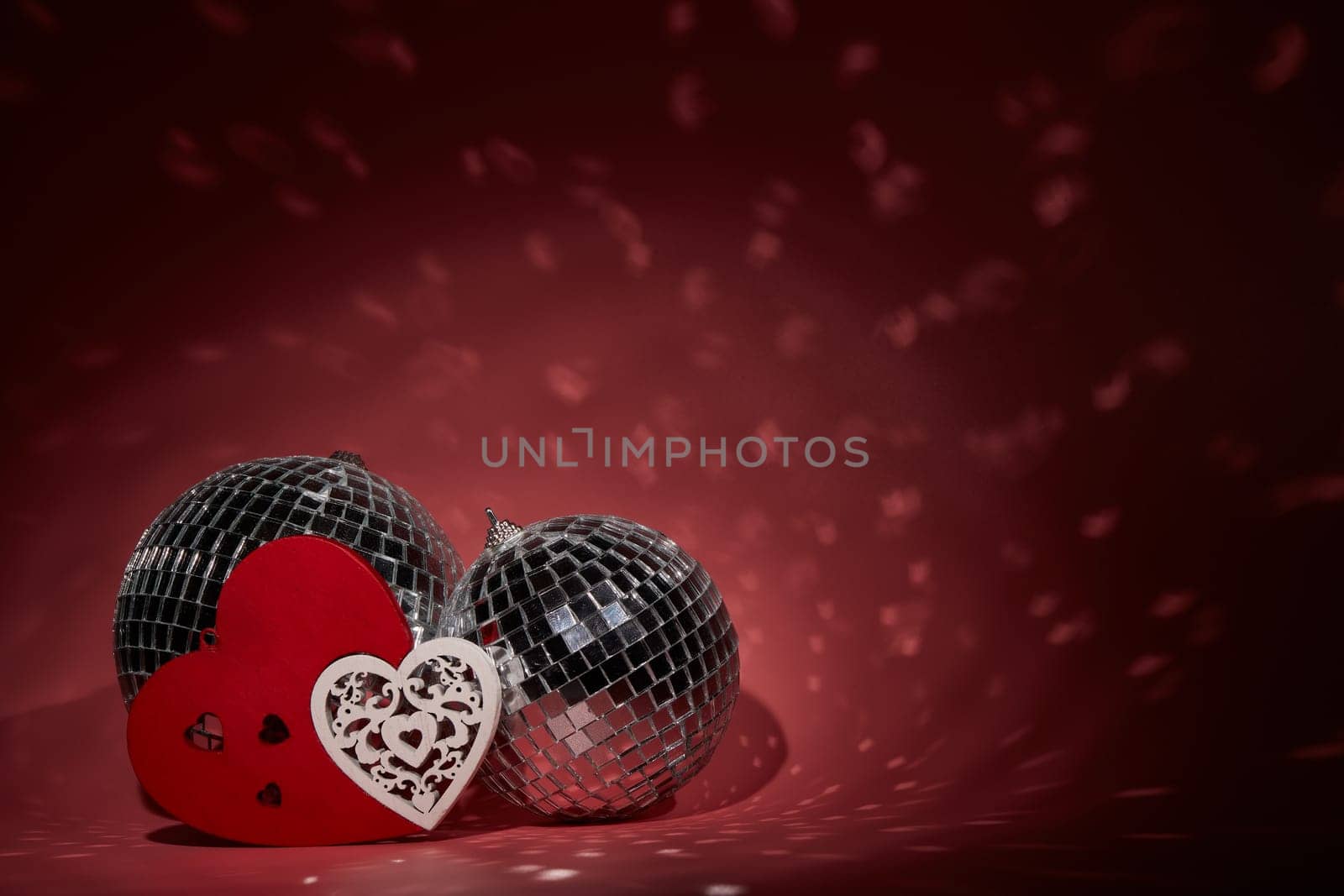 Glittering mirror disco ball  and decorative hearts on dark background with red lighting. Copy space. Valentine's Day background. Holiday party. Nightclub. Entertainment, disco, music show background