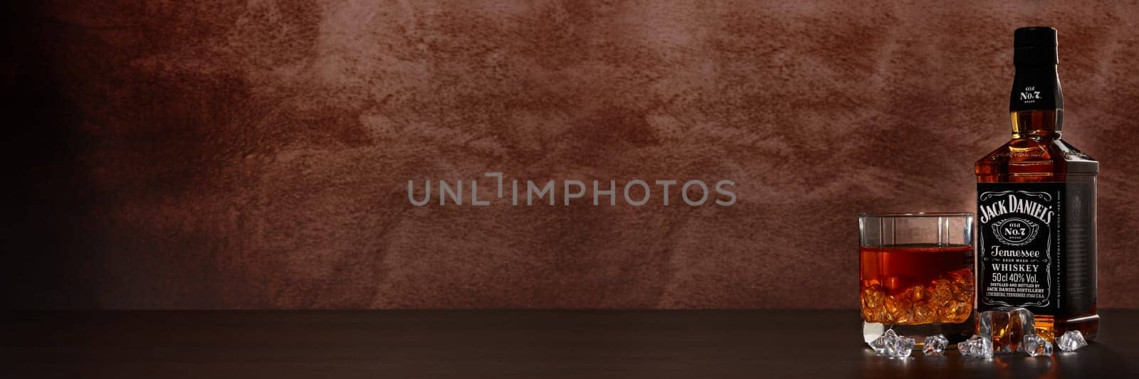 St.Petersburg, Russia - December 2019 - Bottle of Jack Daniel's whiskey and glass with drink and ice on wooden table on brown background with copy space. Extra wide panorama banner background