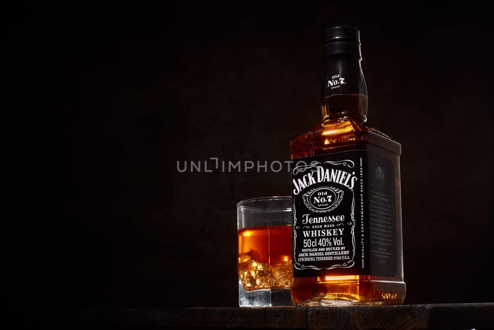 St.Petersburg, Russia - December 2019 - Bottle of Jack Daniel's whiskey and glass with drink and ice  on wooden table on brown background with copy space. Brand of the American whiskey