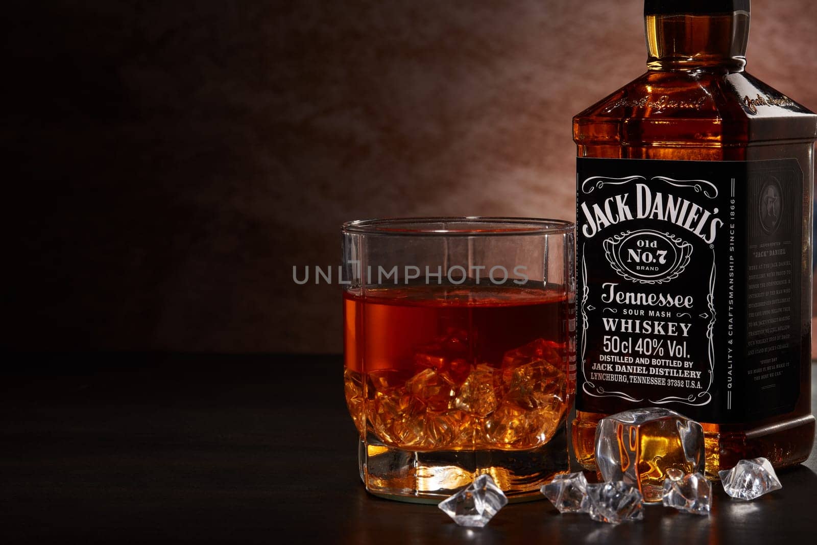 St.Petersburg, Russia - December 2019 - Bottle of Jack Daniel's whiskey and glass with drink and ice  on wooden table on brown background with copy space. Brand of the American whiskey