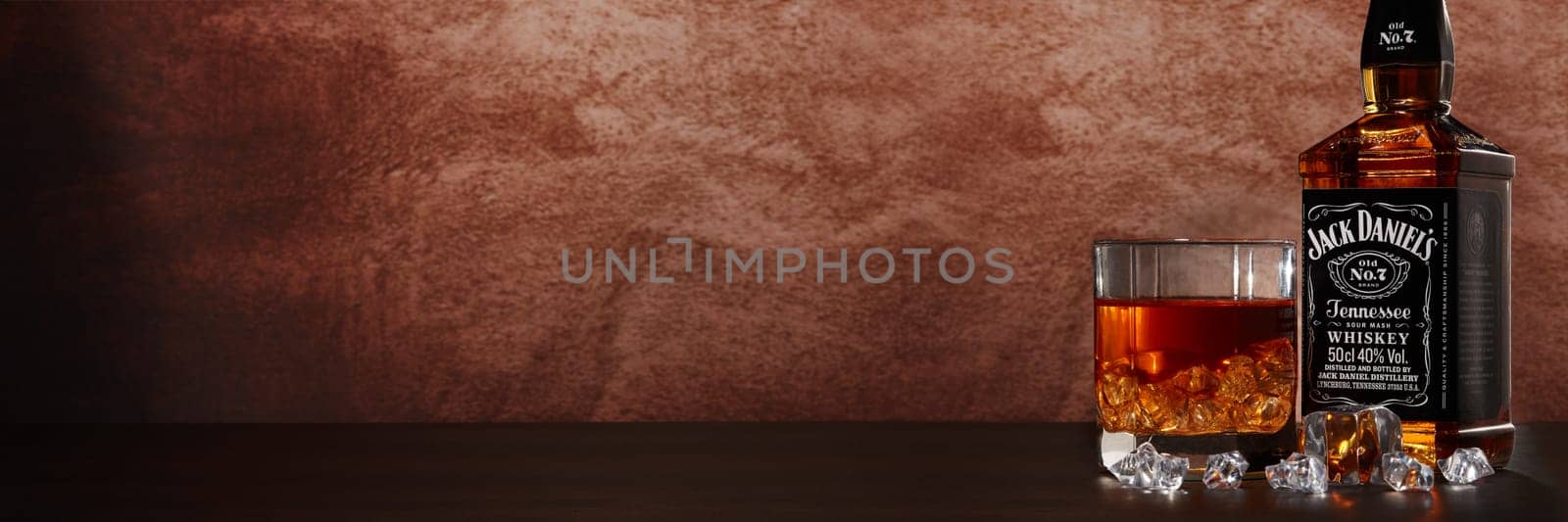 St.Petersburg, Russia - December 2019 - Bottle of Jack Daniel's whiskey and glass with drink and ice on wooden table on brown background with copy space. Extra wide panorama banner background