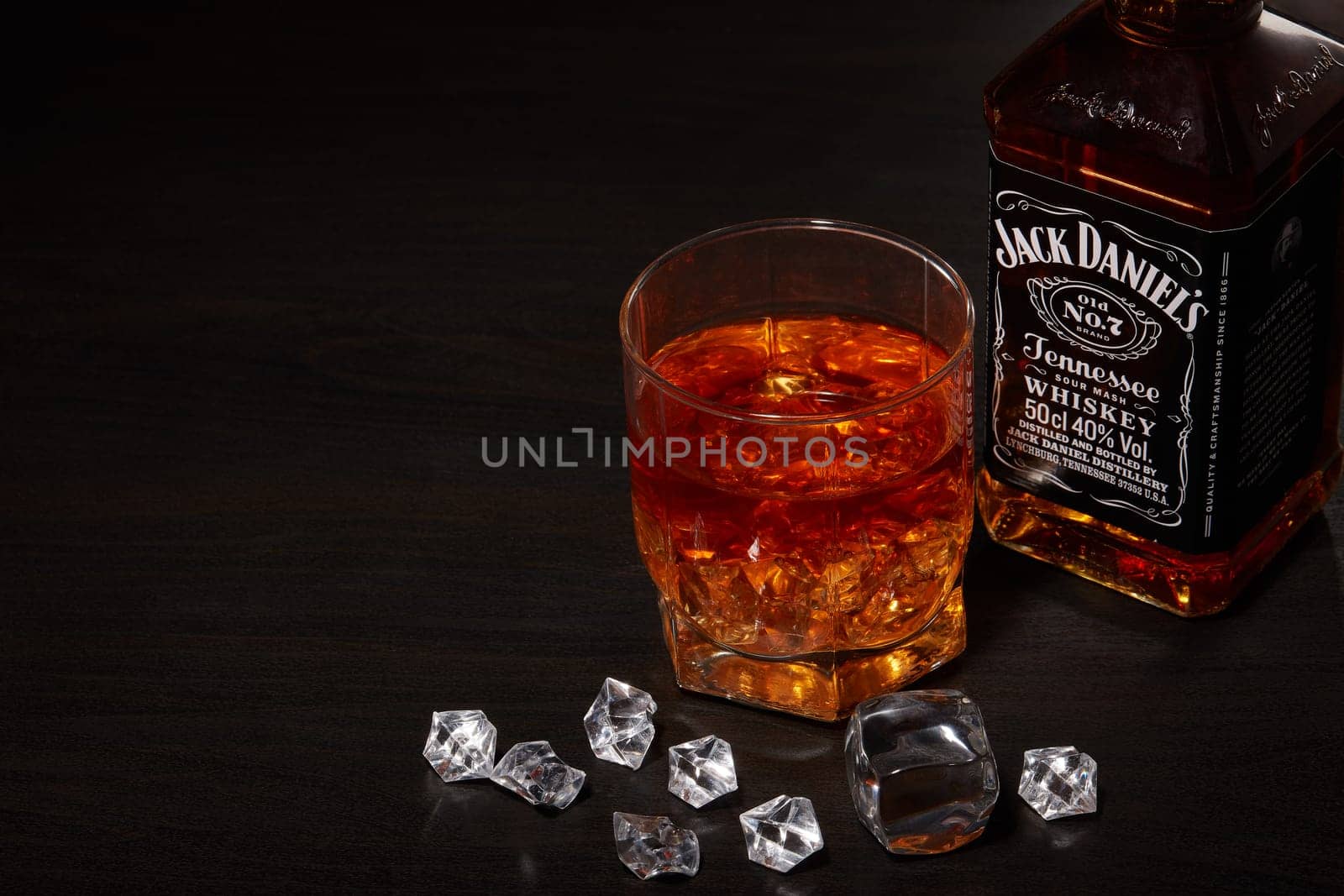 St.Petersburg, Russia - December 2019 - Bottle of Jack Daniel's whiskey and glass with drink and ice  on wooden table on brown background. Brand of the American whiskey