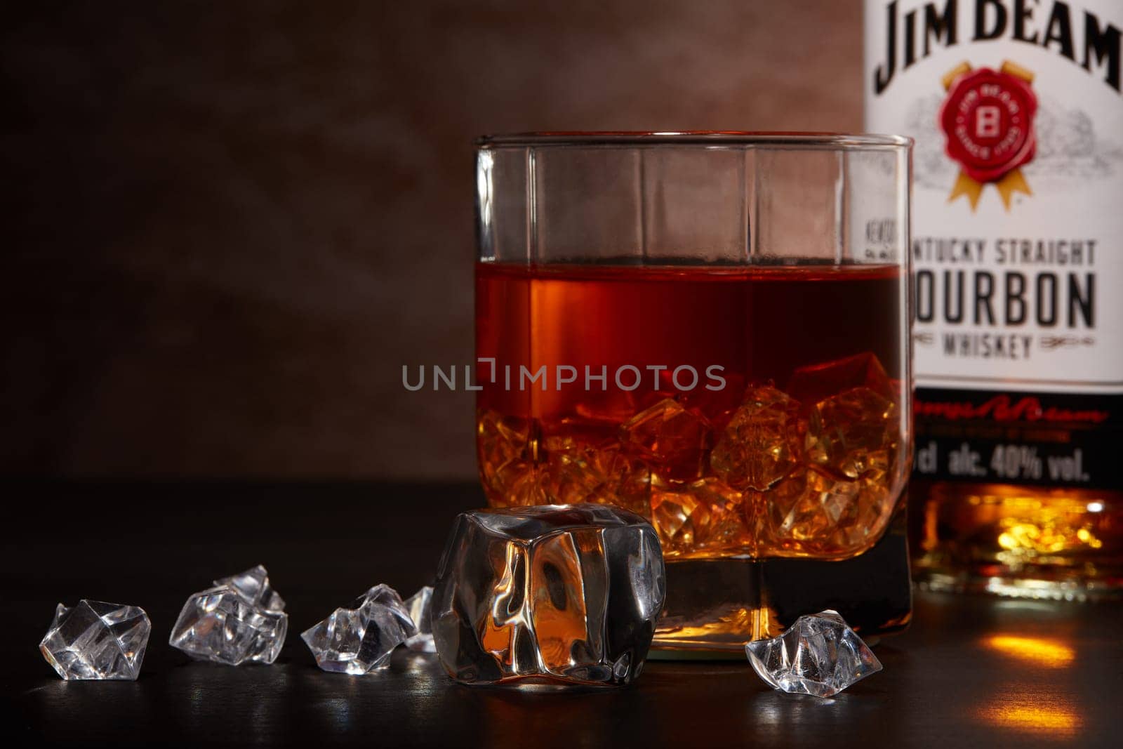 St.Petersburg, Russia - December 2019 - Bottle of Jim Beam bourbon whiskey and glass with drink and ice  on wooden table on brown background. Kentucky straight bourbon whiskey