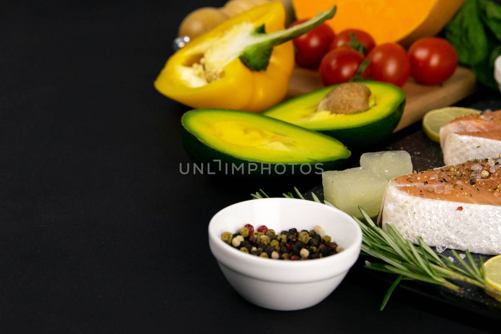 A set of healthy balanced super food, avocado in the foreground, fresh salmon, vegetables, cereals and nuts on a black background. Top view, flat lay