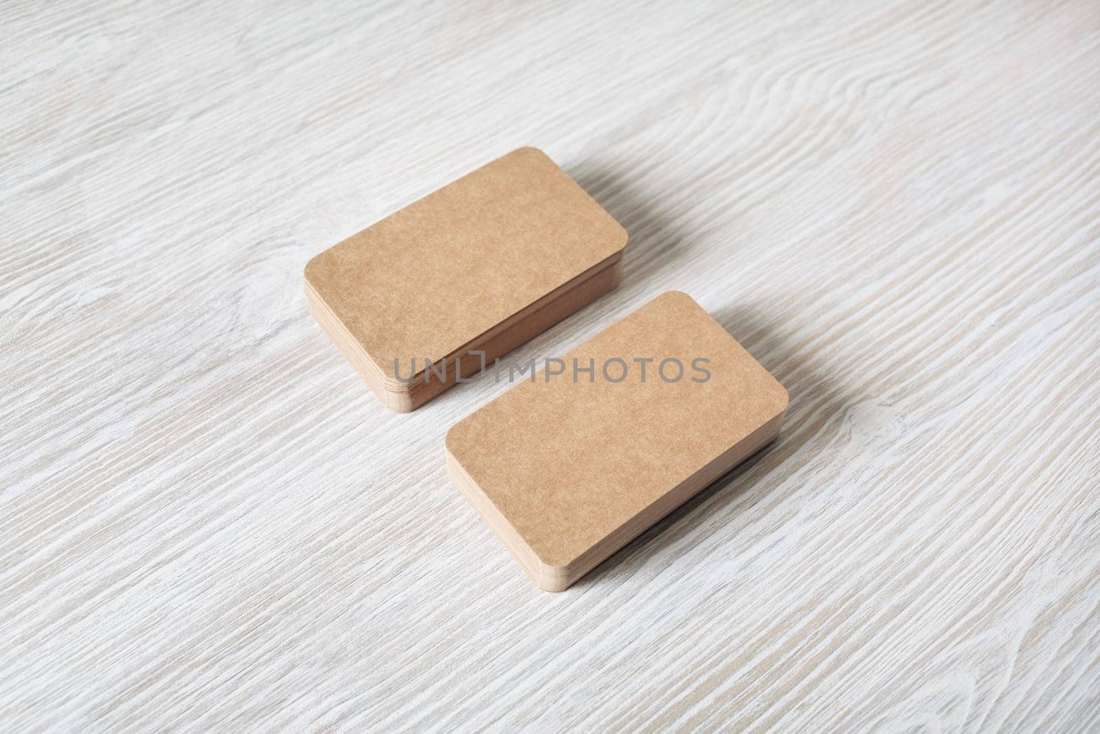 Photo of blank kraft business cards stacks on light wood table background. Template for branding identity.