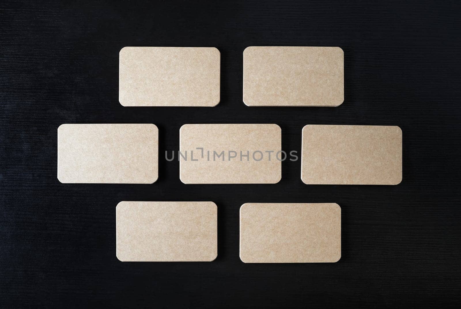 Blank kraft business cards mock-up on black wood table background. Copy space for text. Flat lay.