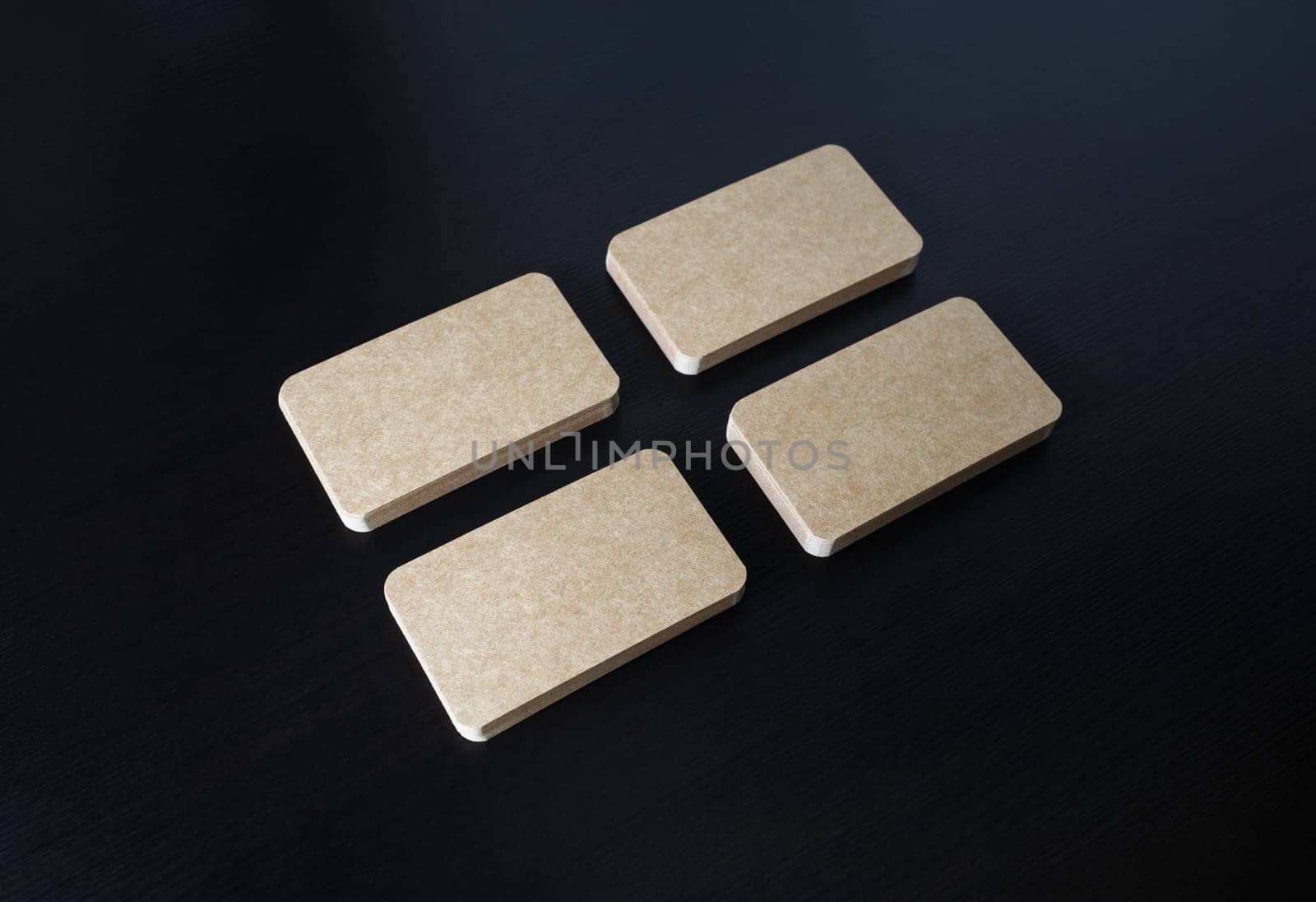 Four piles of blank kraft business cards on black wooden background. Corporate ID template.