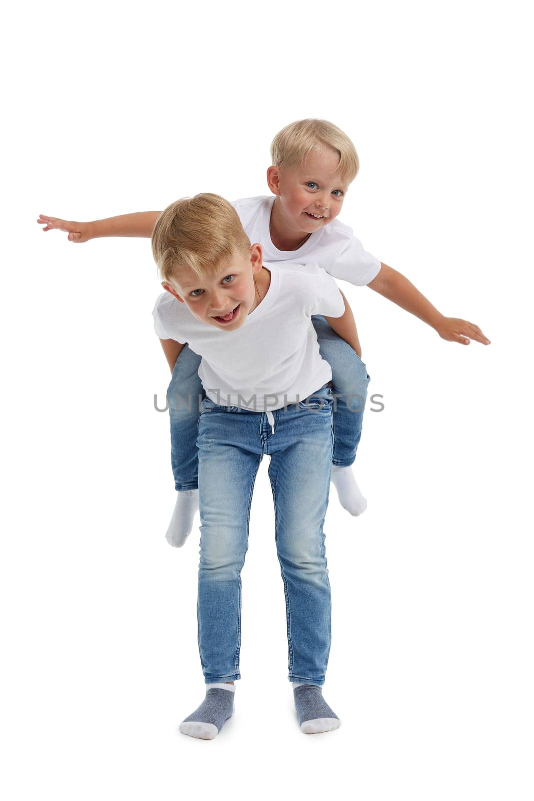Friendly family. Older brother is carrying younger boy  on the back , isolated on a white background. Happy siblings. Two little brothers. Concept of people and family