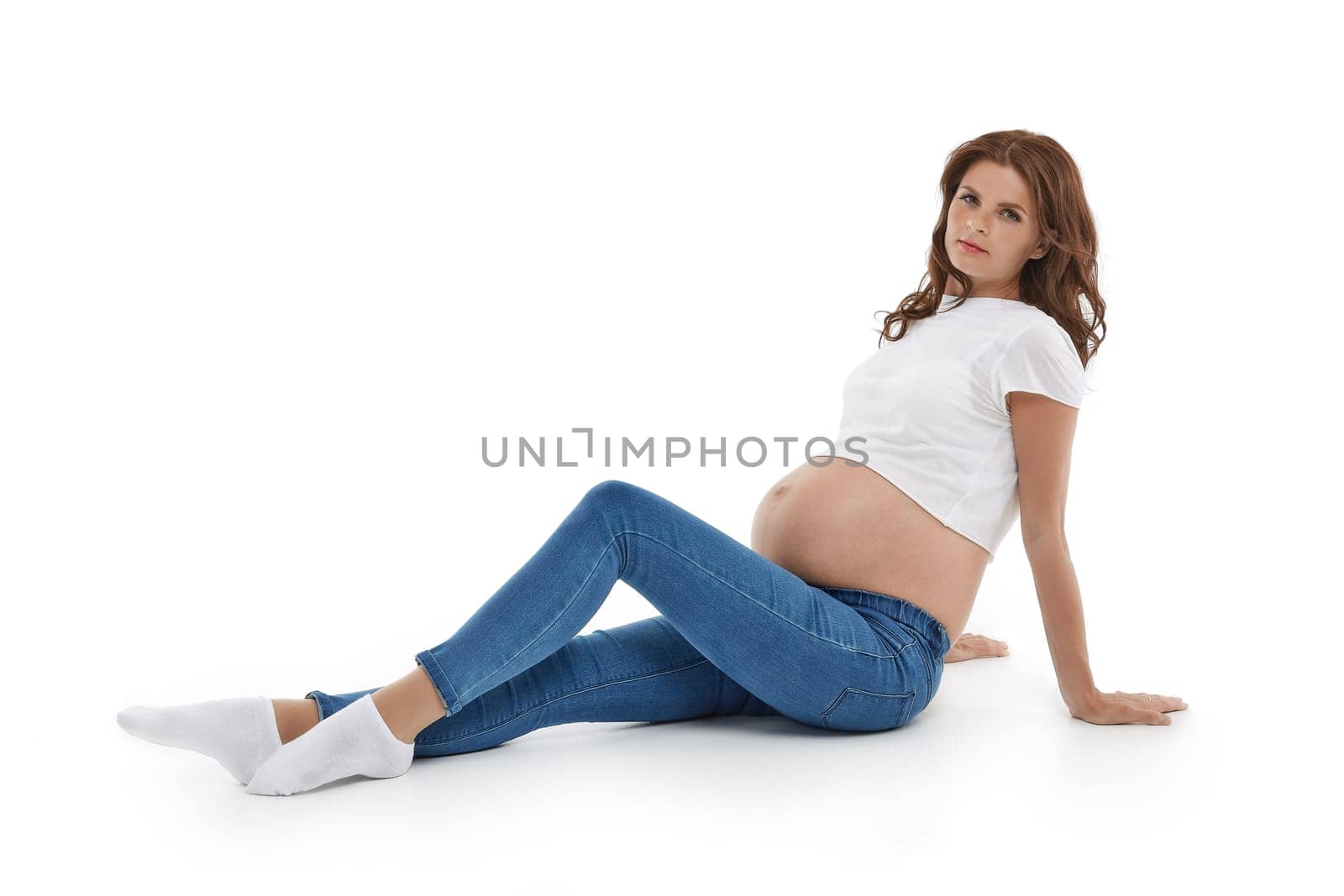 Young pregnant woman is sitting isolated on white background.