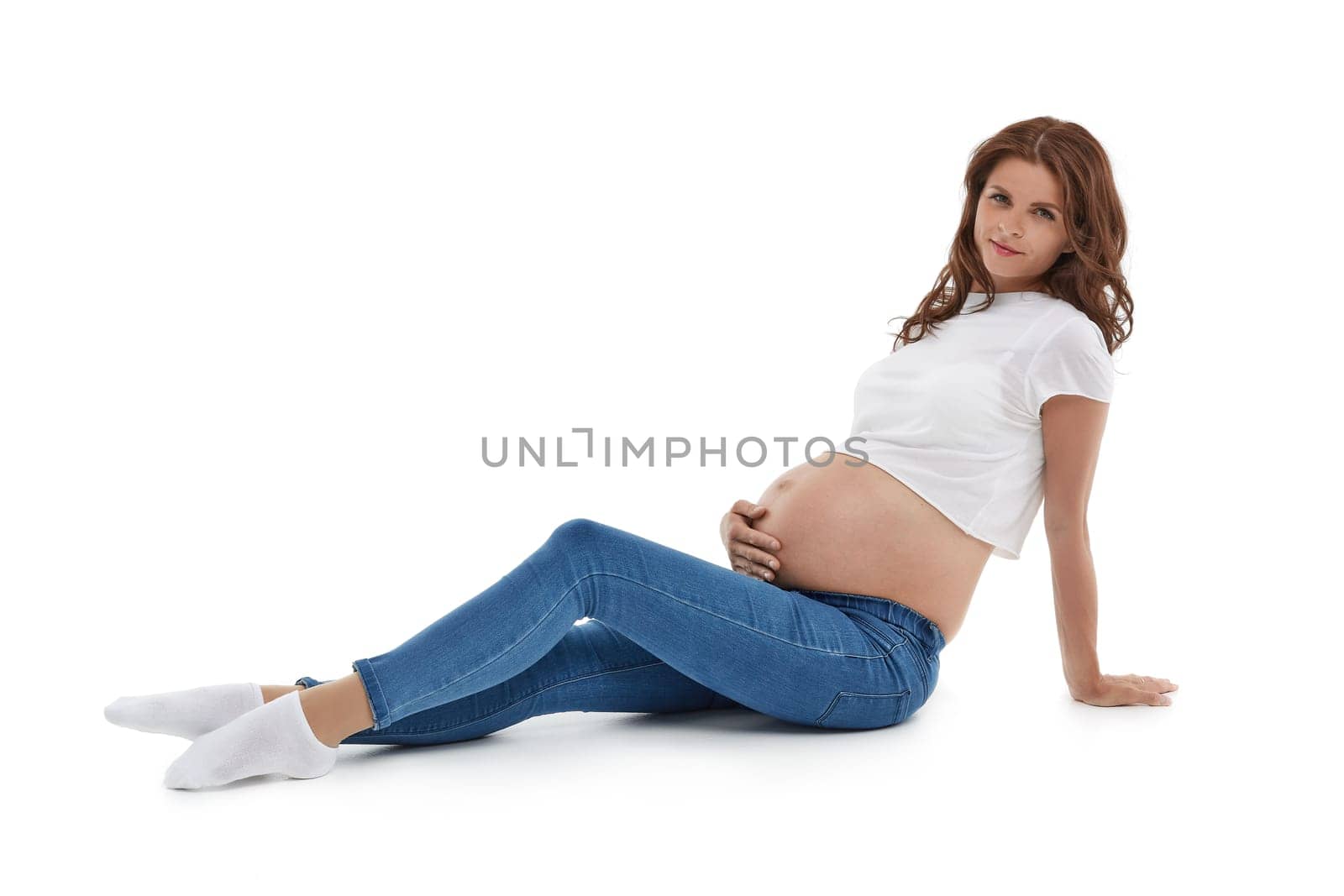 Young pregnant woman is sitting isolated on white background.