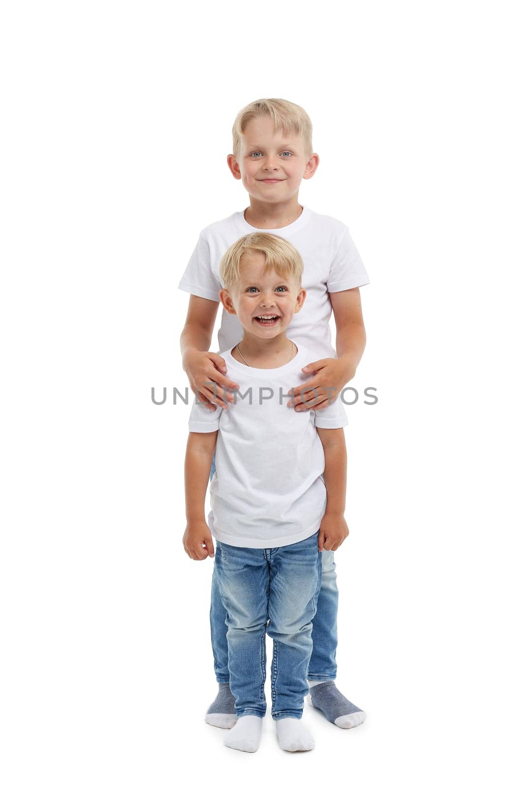 Friendly family. Older brother is hugging younger boy, standing isolated on a white background. Happy siblings. Two little brothers. Concept of people and family