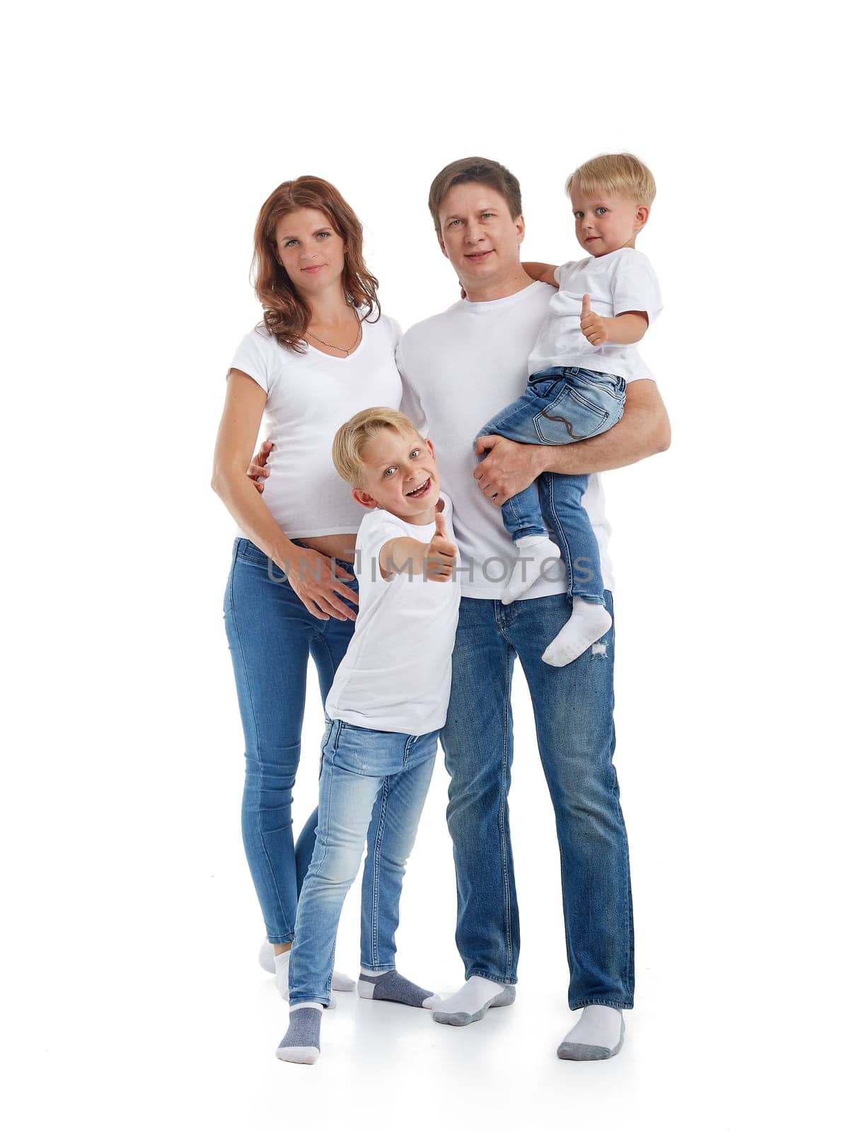 Happy parents: pregnant mother and father with lovely two sons are stand hugging and smiling, isolated on a white background. Happy friendly family. Concept of people and family