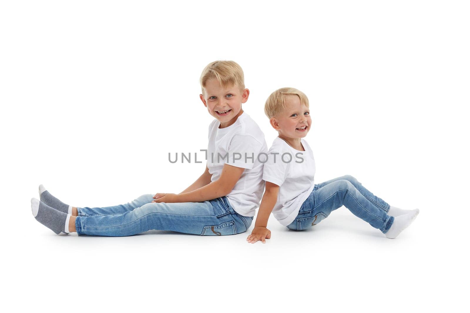 Friendly family. Older brother and younger boy are sitting with backs to each other isolated on a white background. Happy siblings. Two little brothers. Concept of people and family