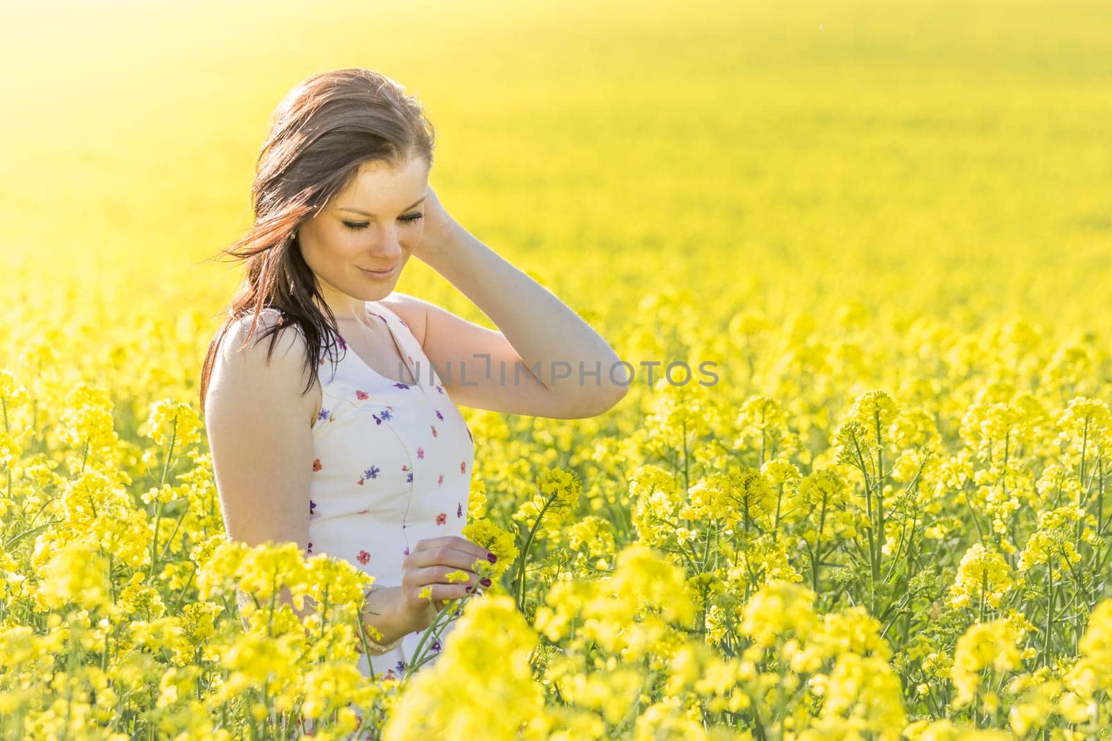 Beautiful girl eyes closed in yellow flowers field infinite horizon. Sunny sun sunshine and authentic lifestyle in windy weather hair.