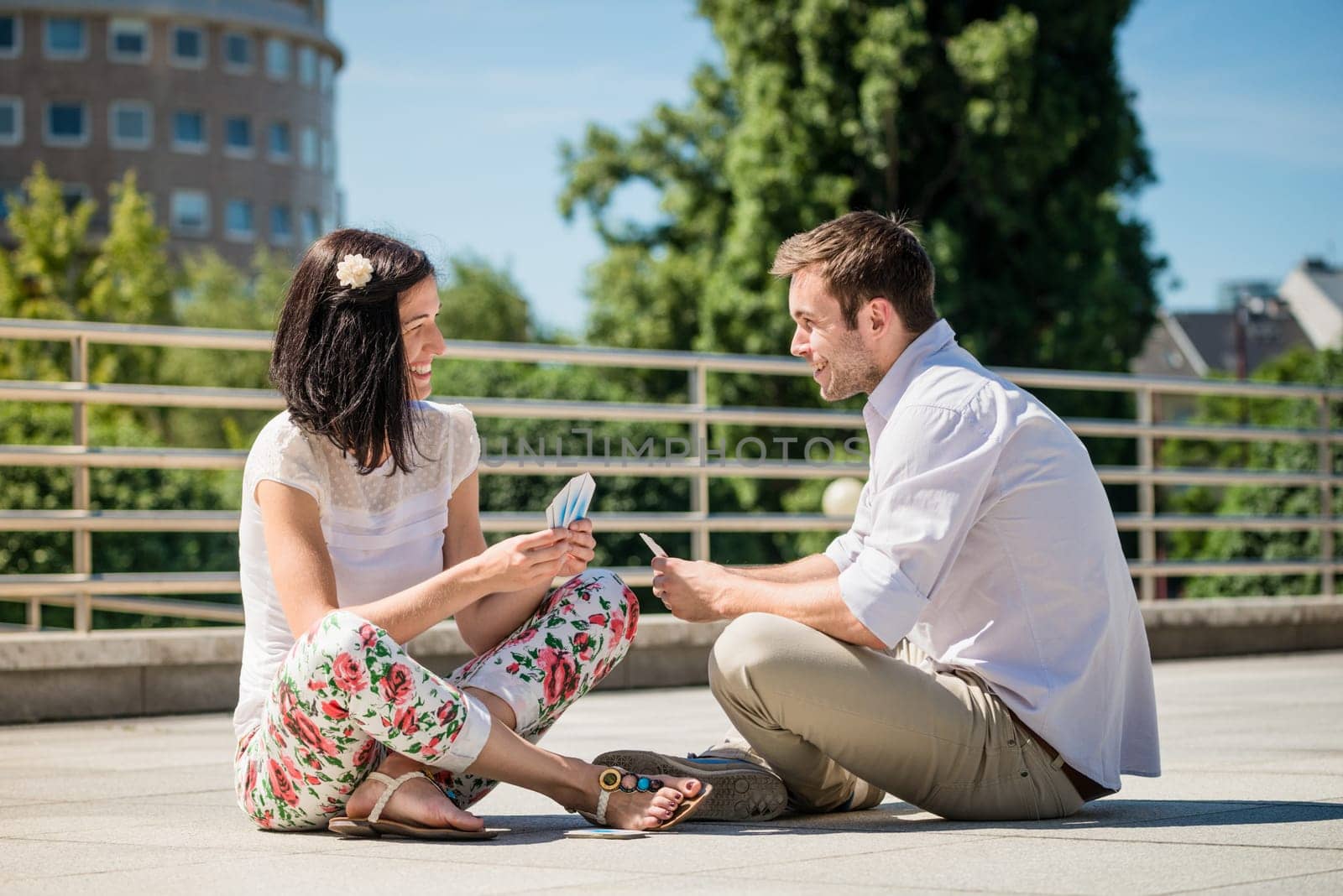 Young couple playing cards outdoor sitting on ground