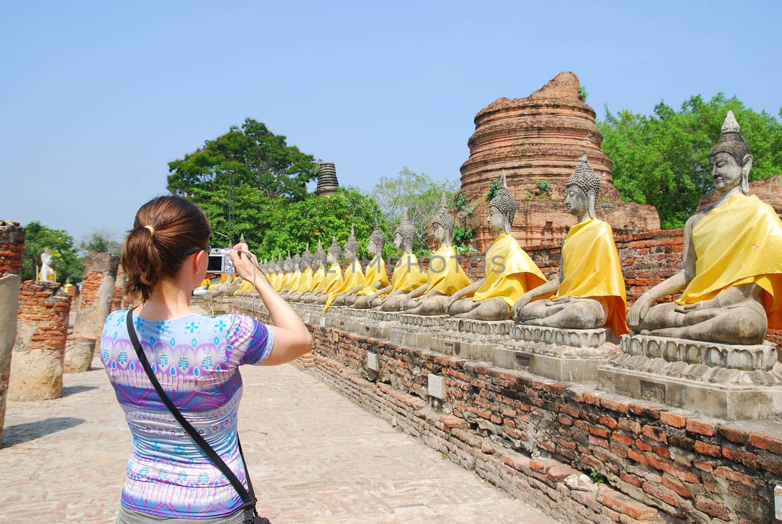 Tourist (young woman) taking picture of siting budha statues in Ayutthaya, Thailand