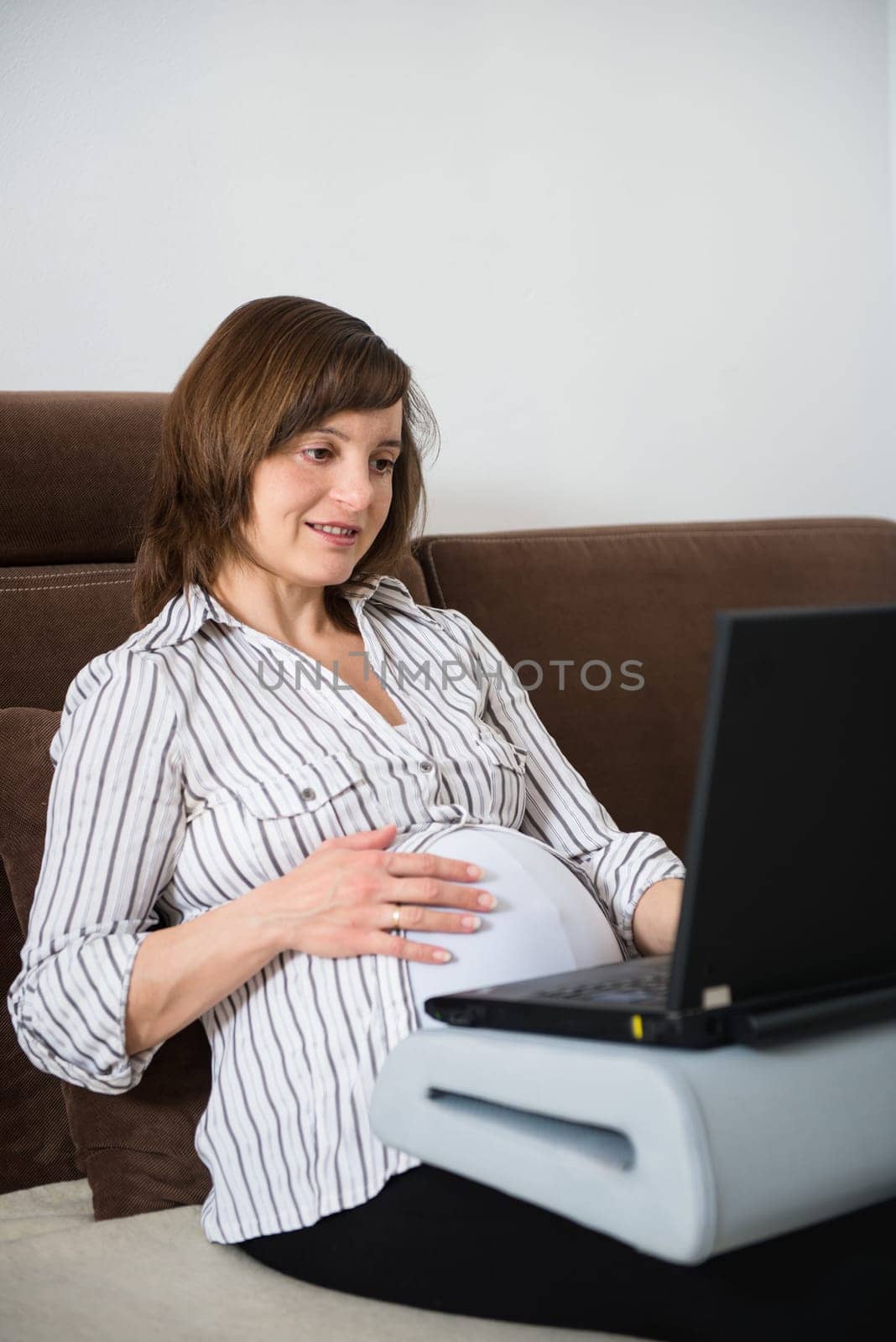 Pregnant woman working on laptop from home on sofa