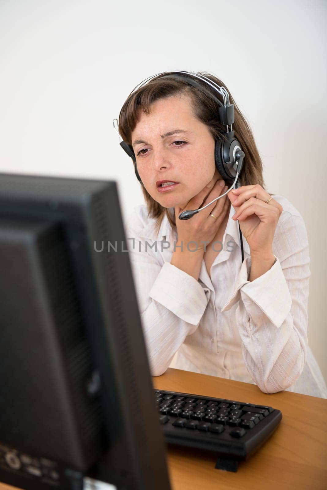 Young ill business woman with throat pain working with computer and headset