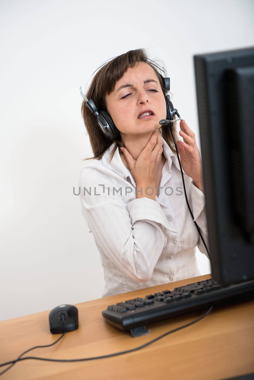 Young ill business woman with throat pain working with computer and headset