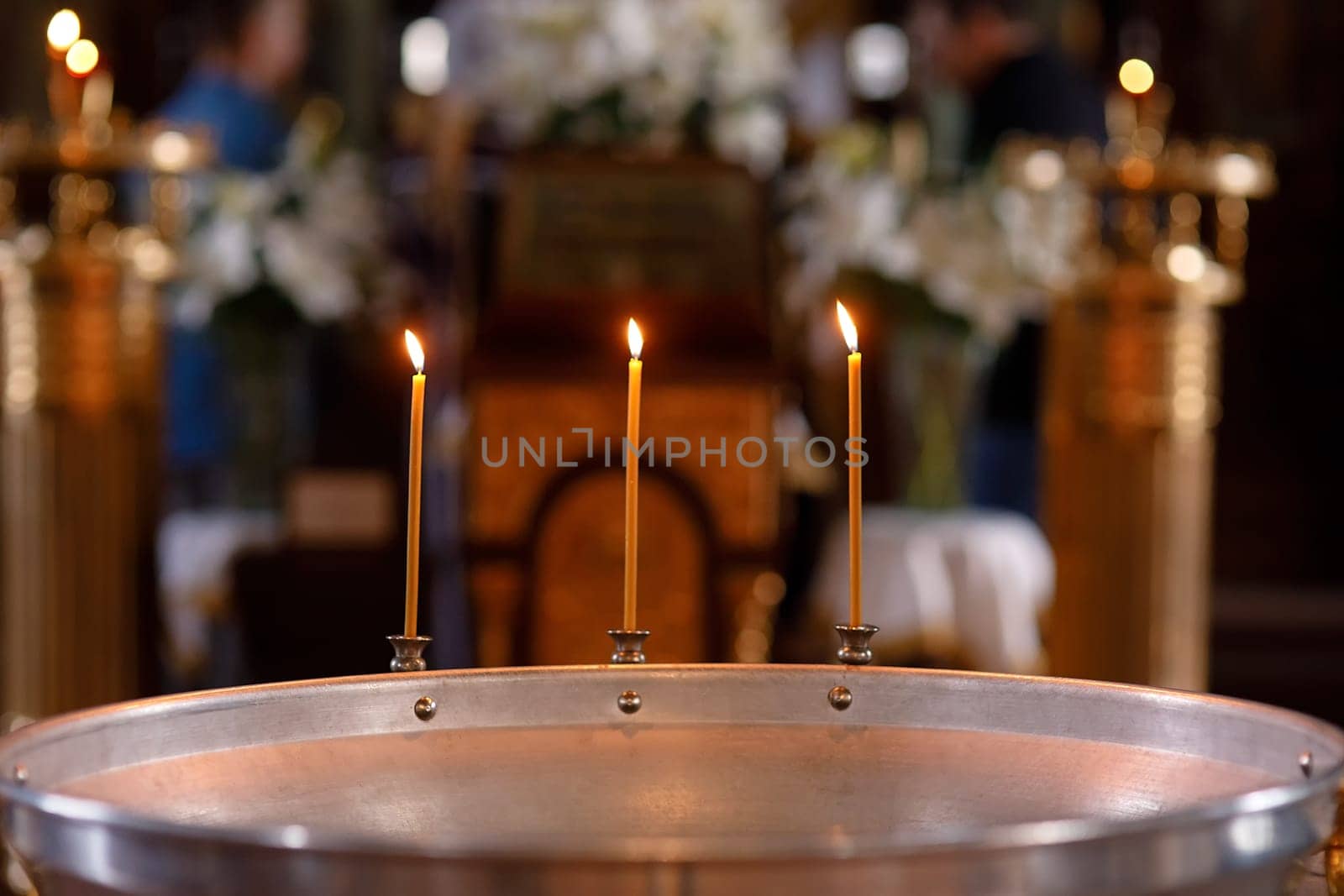 Three burning candles on a font for baptism in a church on the background of the altar in the hall