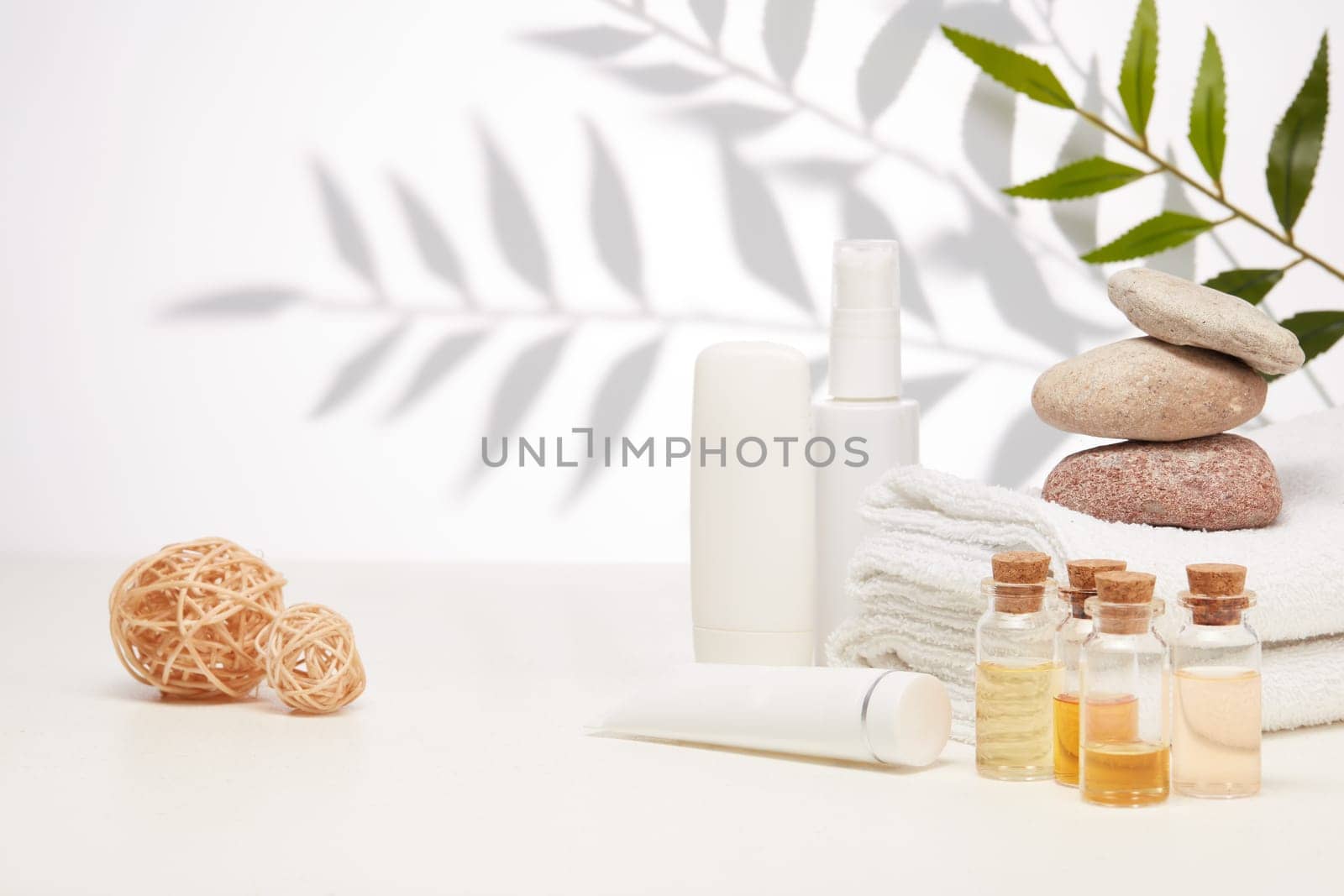 Spa still life with creams, essential oils, stones and towels on light background with shadow from plant. Healthy lifestyle, body care, Spa treatment.