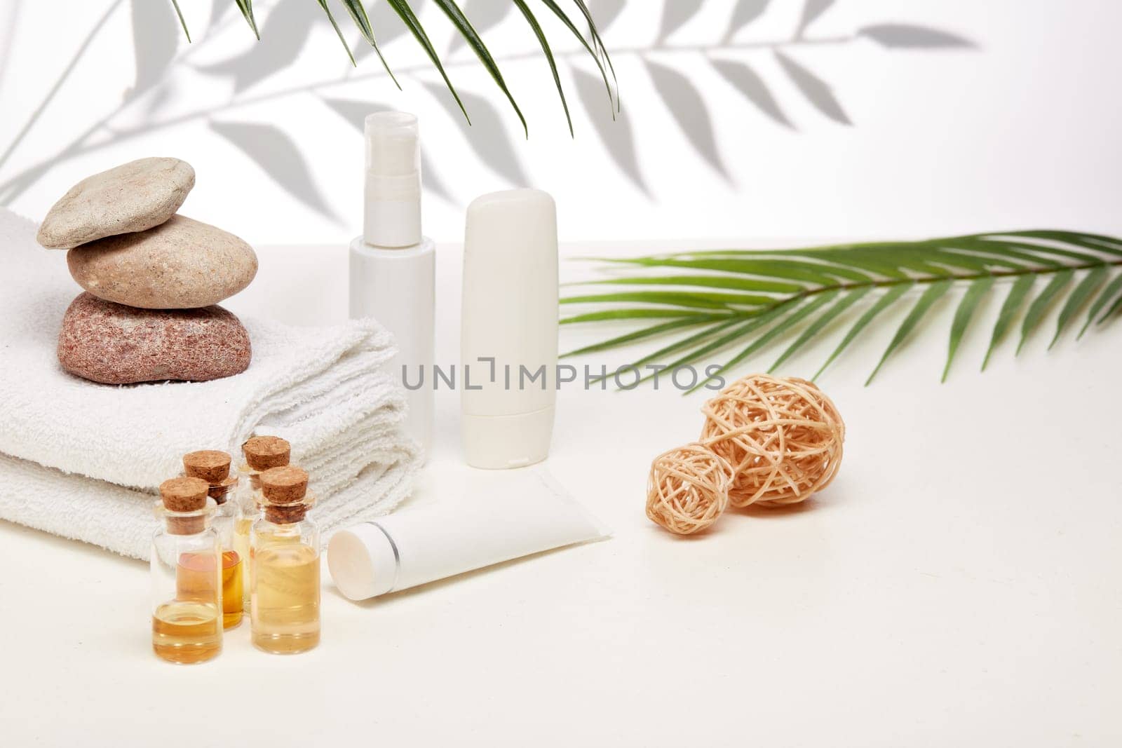 Spa still life with creams, essential oils, stones and towels on light background with shadow from plant. Healthy lifestyle, body care, Spa treatment.