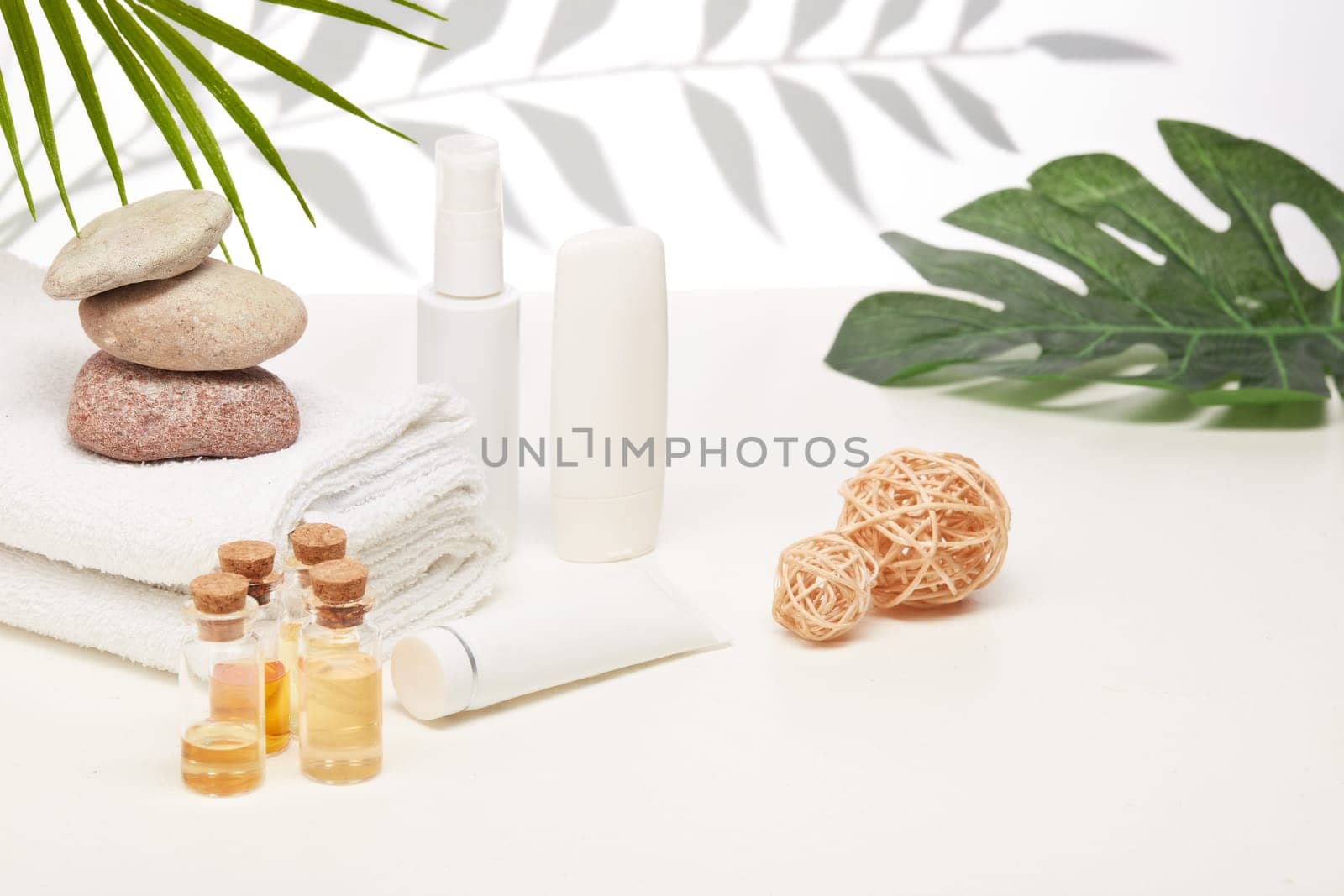 Spa still life with creams, essential oils, stones and towels on light background with shadow from plant. Healthy lifestyle, body care, Spa treatment.