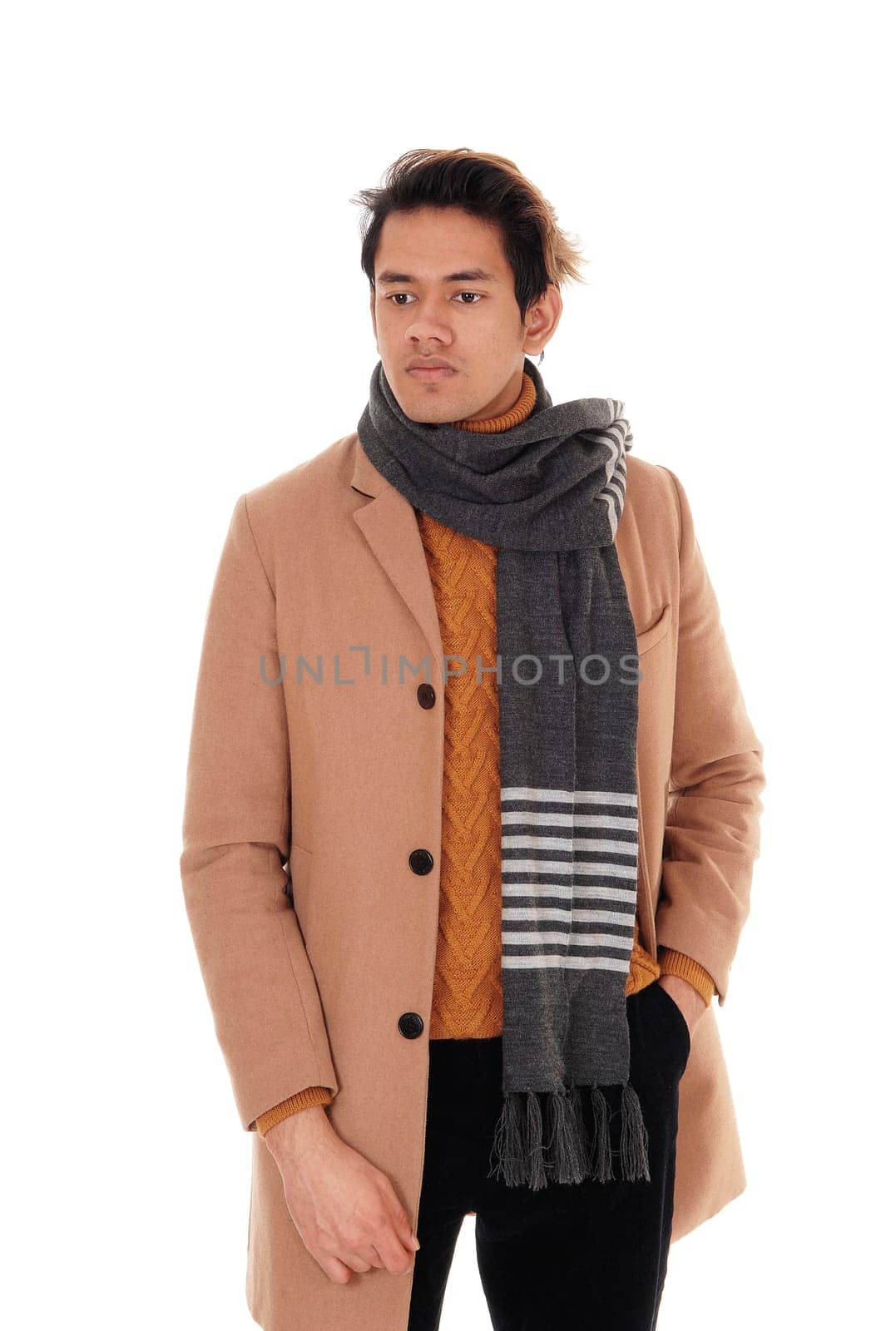 A handsome young man standing in the studio in a beige winter coat.and big scarf, looking away, isolated for white background.