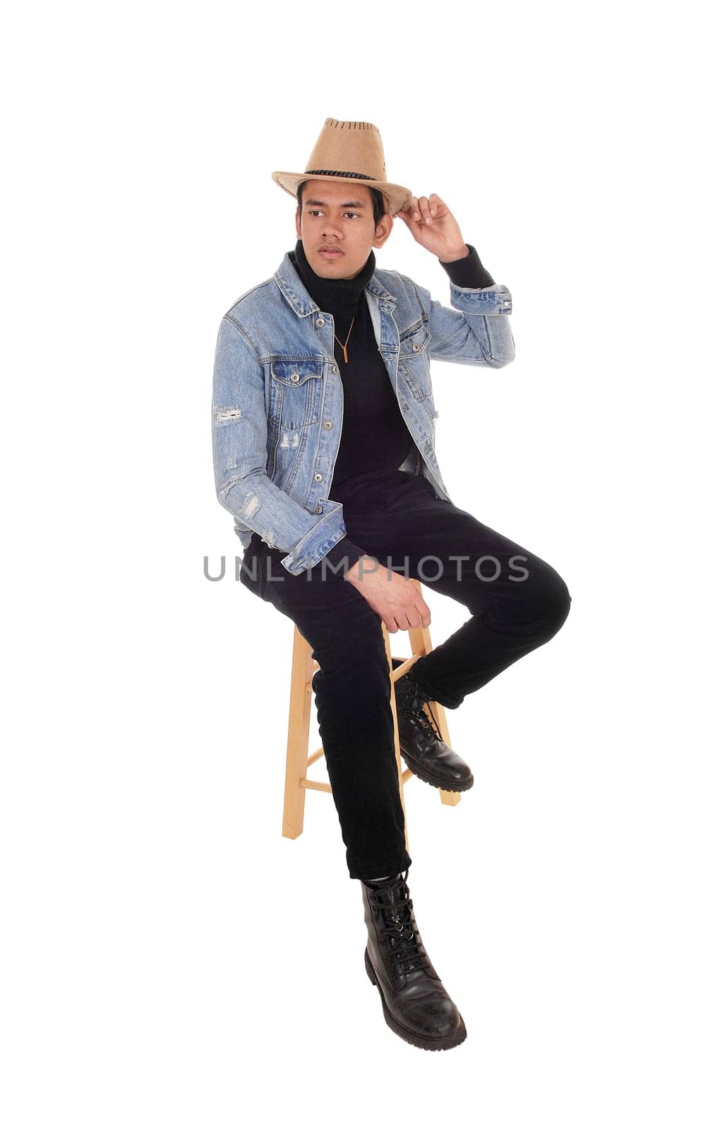 A handsome young man siting on a chair with a jeans jacket and .cowboy hat and black pants, isolated for white background.