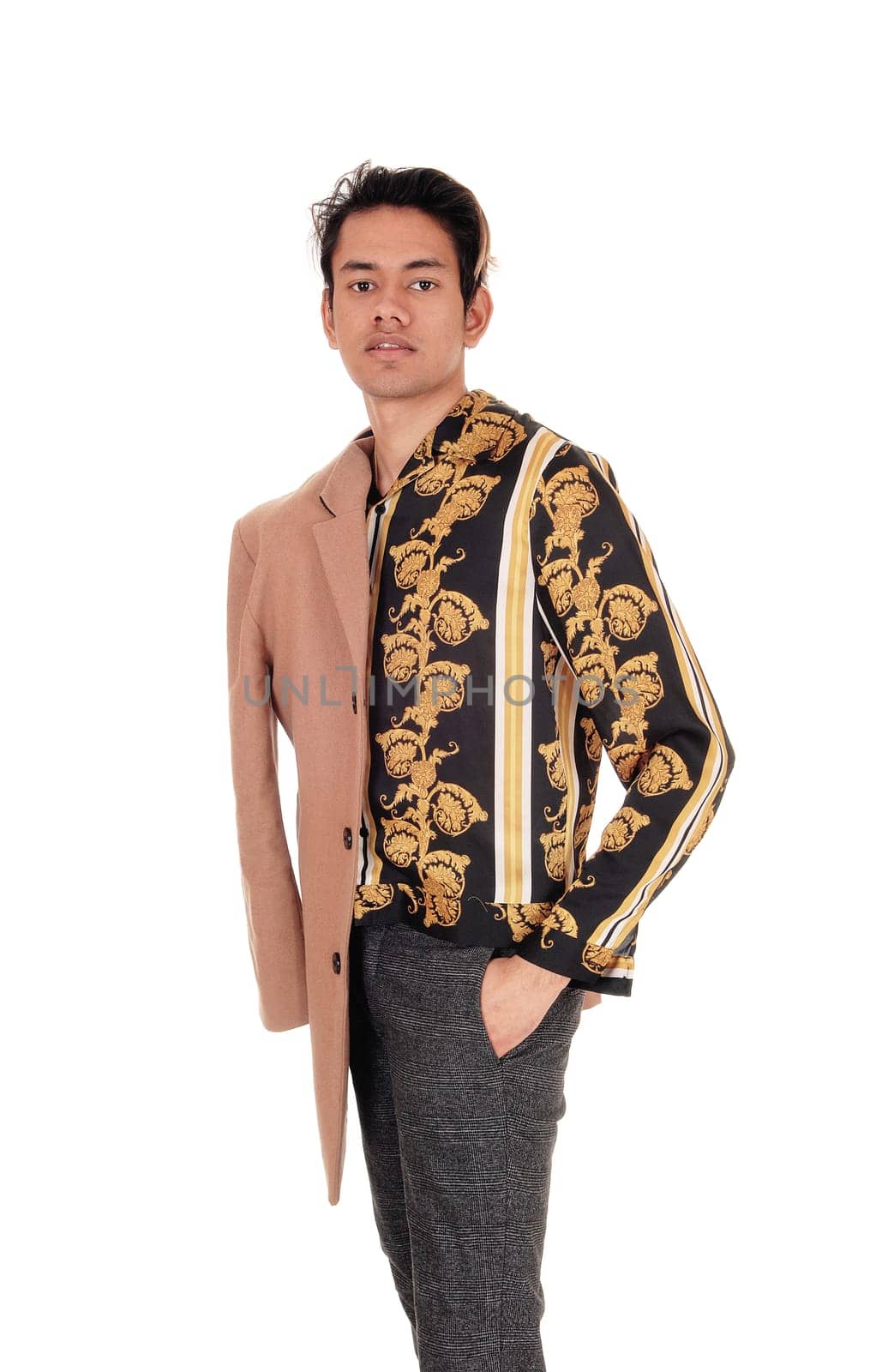 A tall skinny young man in a gold printed shirt and his hand in his.pocket, with beige coat over his shoulder, isolated for white background.