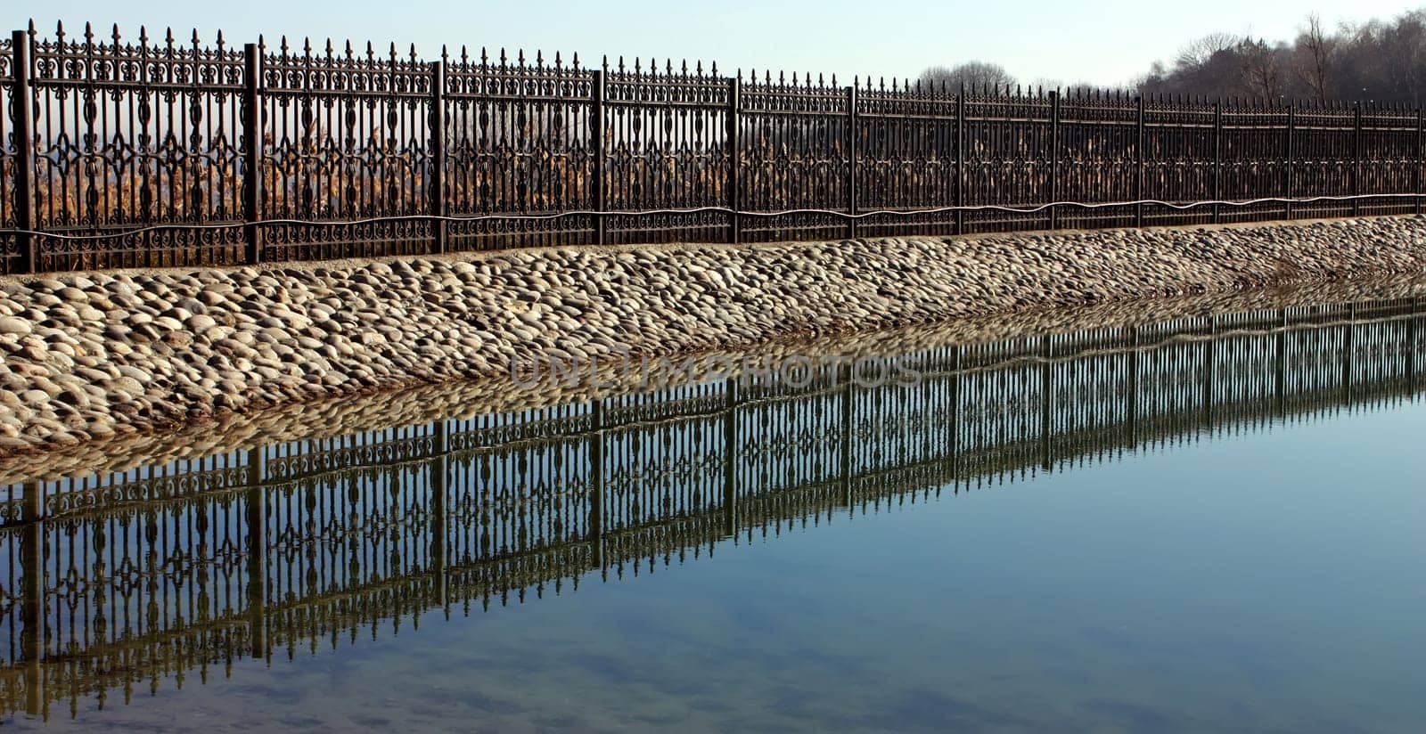 .A beautiful openwork metal fence near a decorative pond.