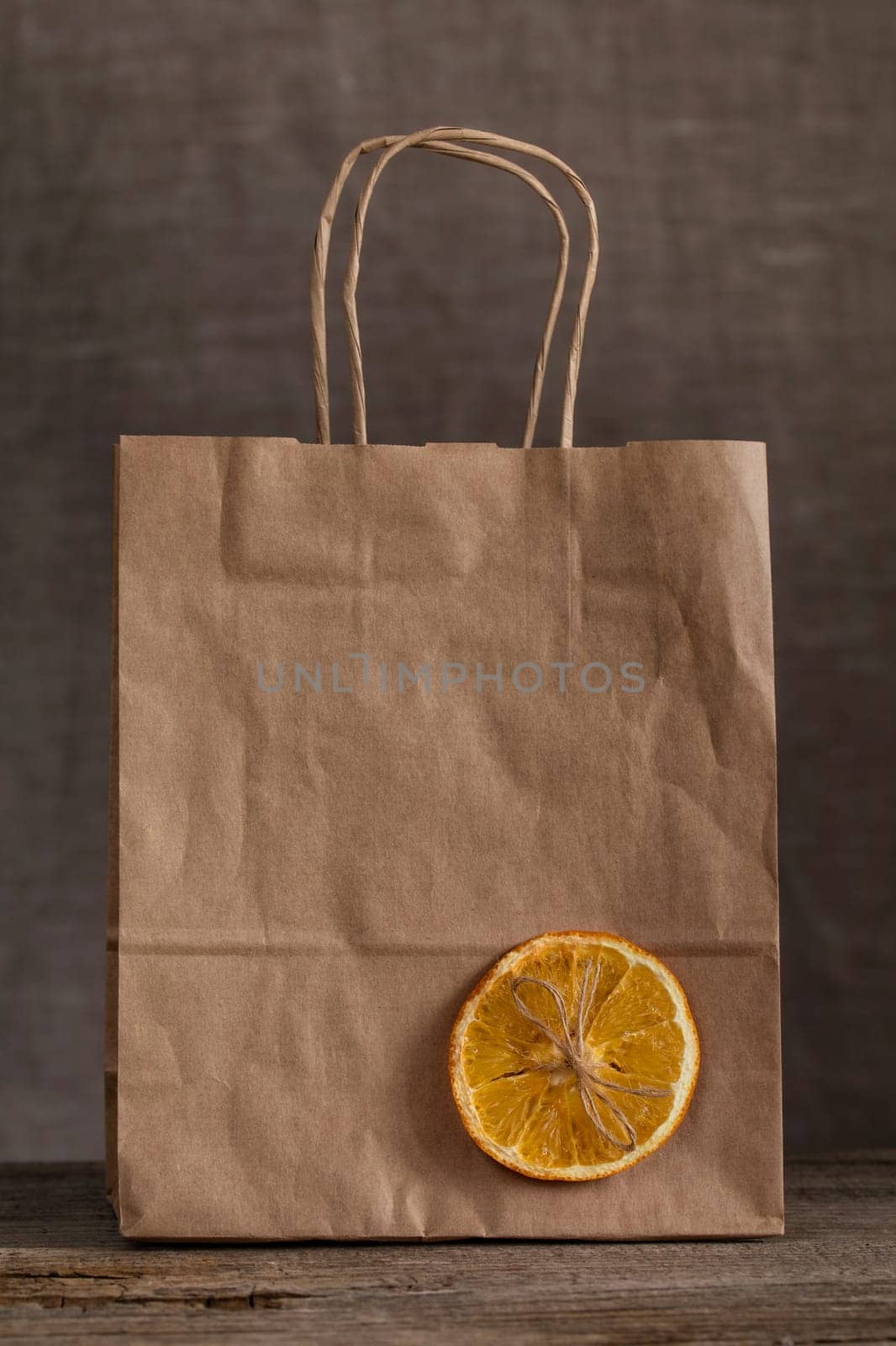 Eco-friendly paper bag on a wooden table, decorated with a slice of dry orange and a bow from a rope