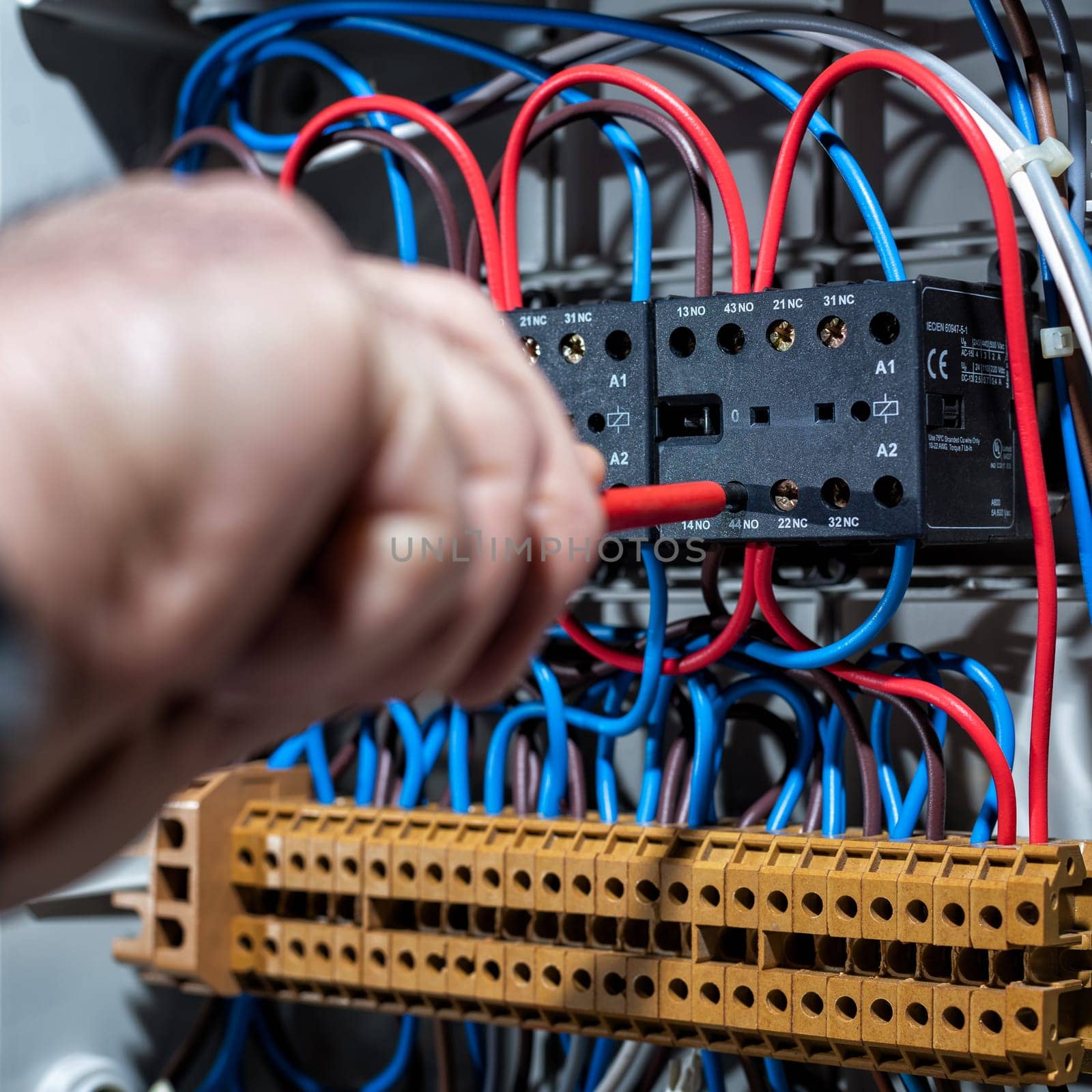 Electrician with screwdriver fixes the cable in a residential electrical distribution panel. Construction industry, electrical system.