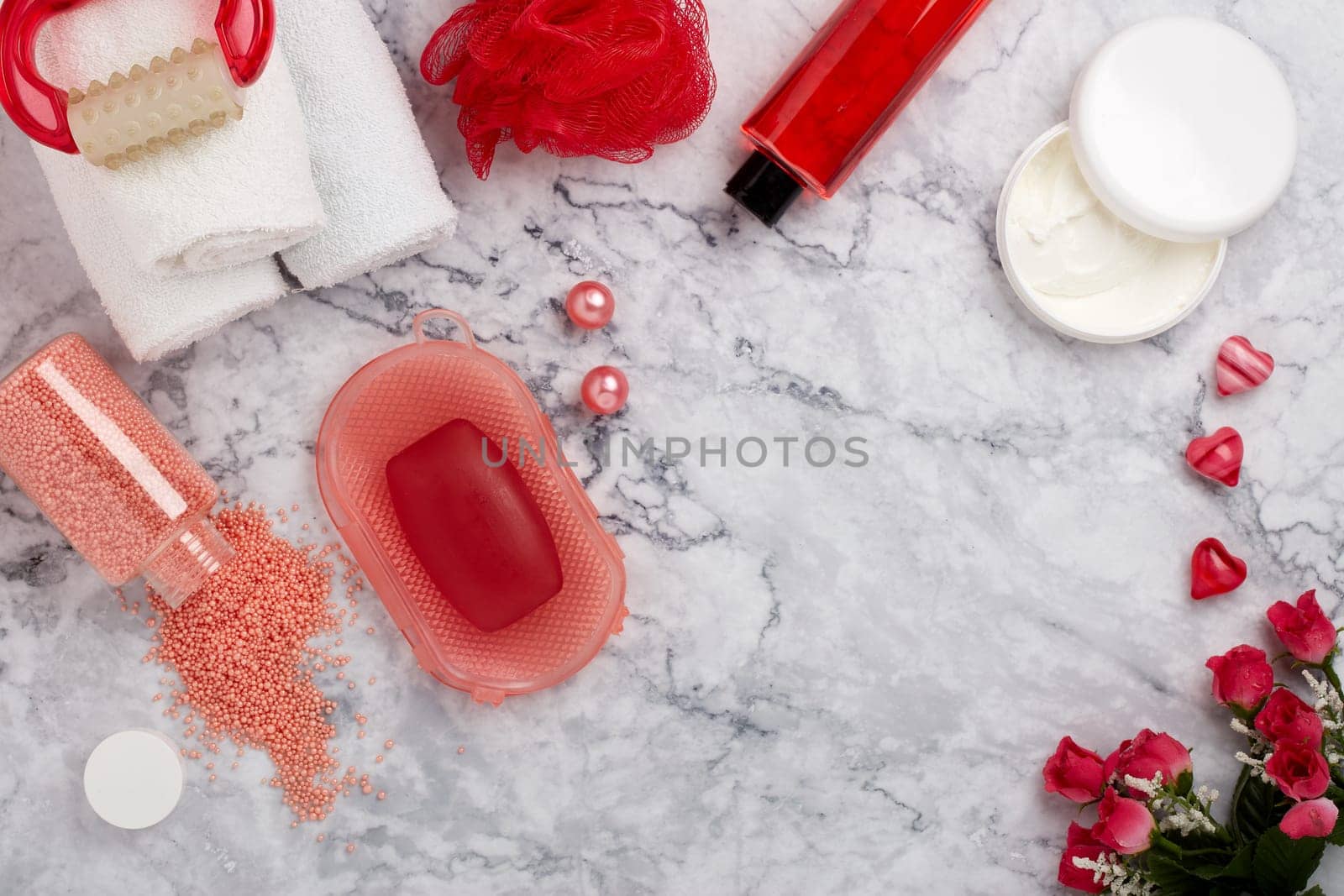 Spa still life with  toiletry, cream,  towel, masager, hearts  and flowers on light  gray marble background. Top view with copy space. Healthy lifestyle, body care, Spa treatment. Valentine