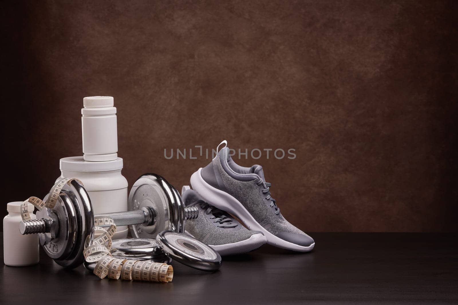 White plastic containers with sports nutrition (supplements), measuring tape, sneakers, dumbbells on dark background with copy space. Fitness, bodybuilding, slimming, sport, healthy lifestyle concept.