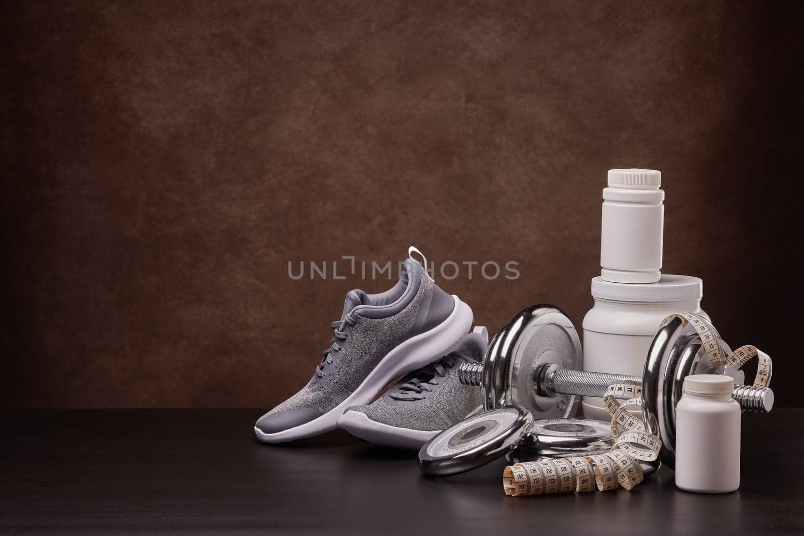 White plastic containers with sports nutrition (supplements), measuring tape, sneakers, dumbbells on dark background with copy space. Fitness, bodybuilding, slimming, sport, healthy lifestyle concept.
