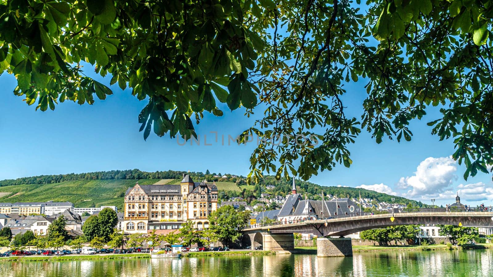 BERNKASTEL-KUES, RHINELAND-PALATINATE, GERMANY – SEPTEMBER 10 2019: Bernkastel-Kues bridge and the Hotel Drei Konige (Three Kings) building at the Moselle river bank on a sunny day.