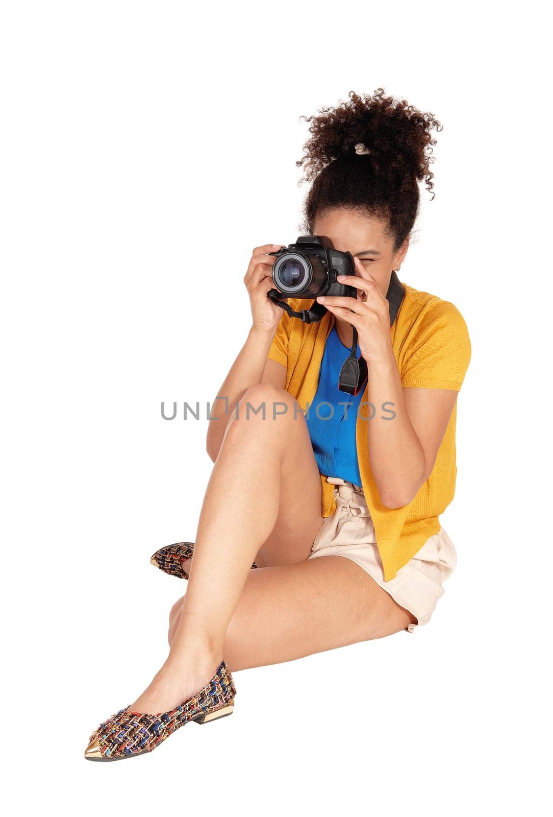 A young multi-racial woman sitting and taking some pictures with her.camera, with her curly black hair, isolated for white background.