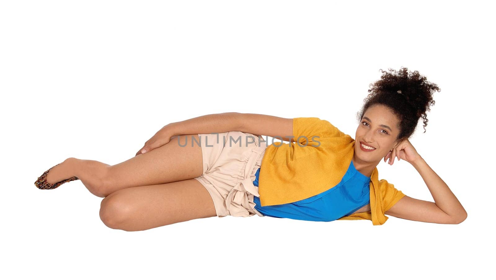 A beautiful multi-racial woman lying on her site on the floor in a yellow.sweater and beige shorts with her curly black hair in a bun on her head,.isolated for white background.