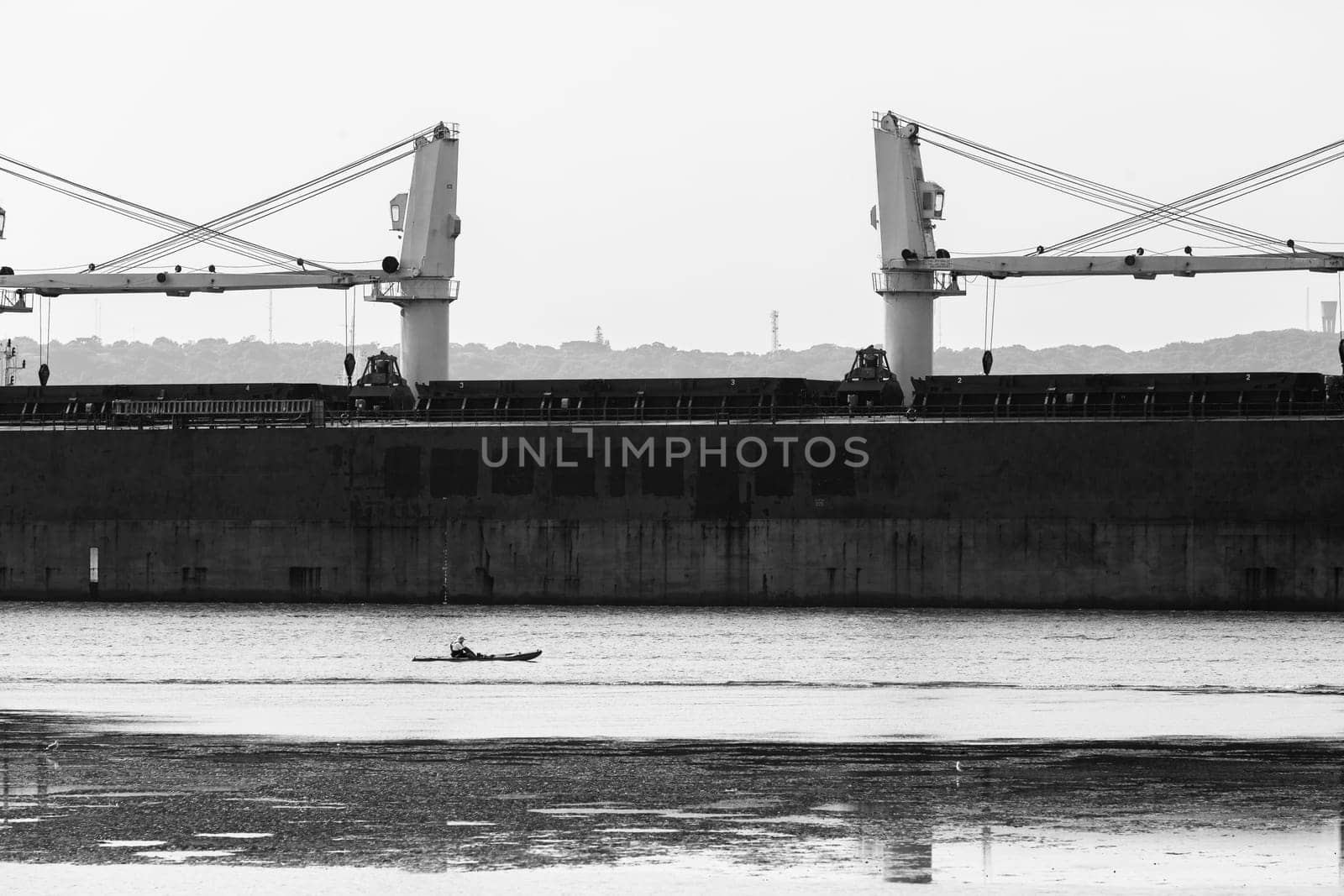 Large ship in channel passes small fisherman on canoe