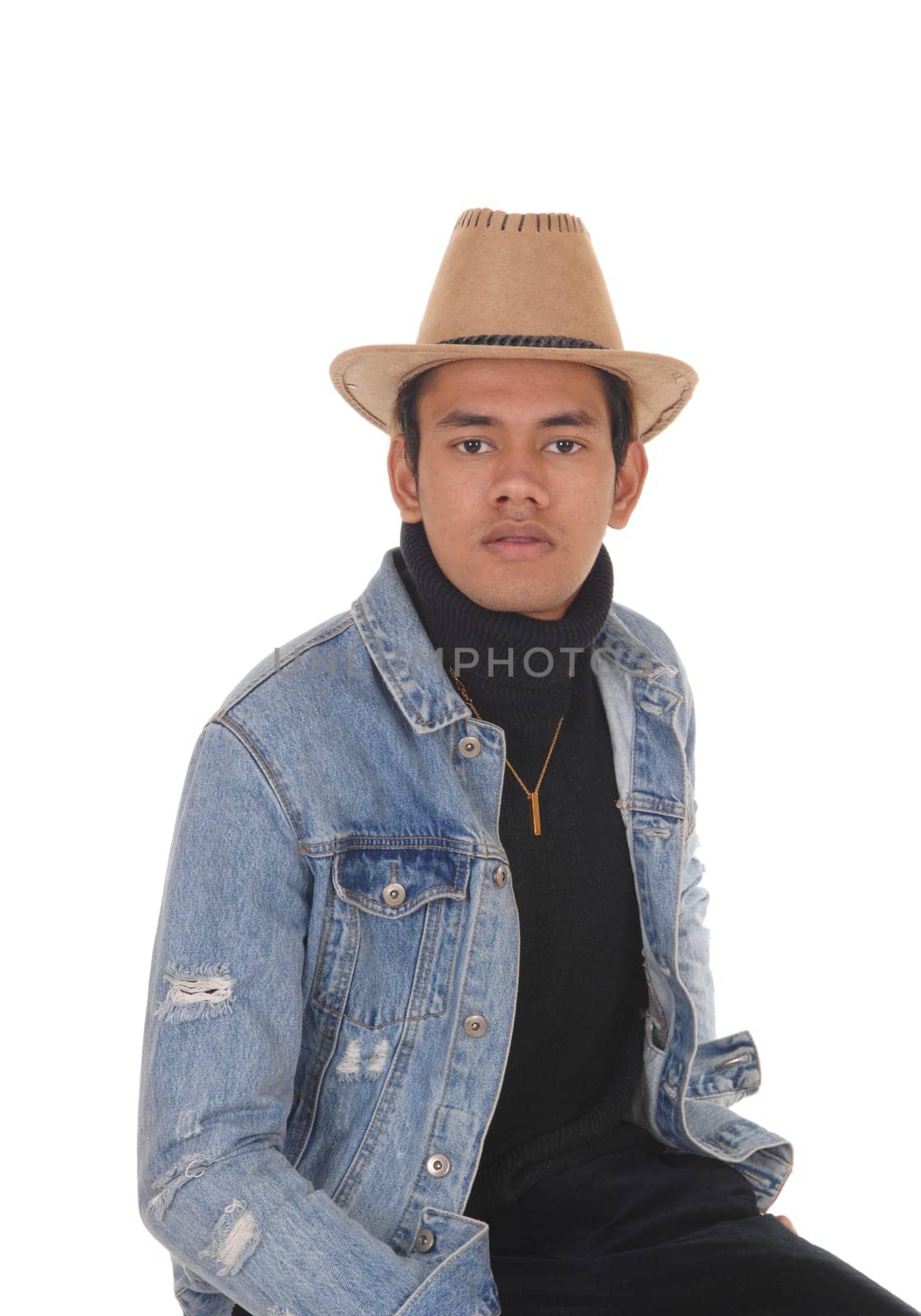 A handsome young man siting on a chair with a jeans jacket and .cowboy hat and black pants, isolated for white background.